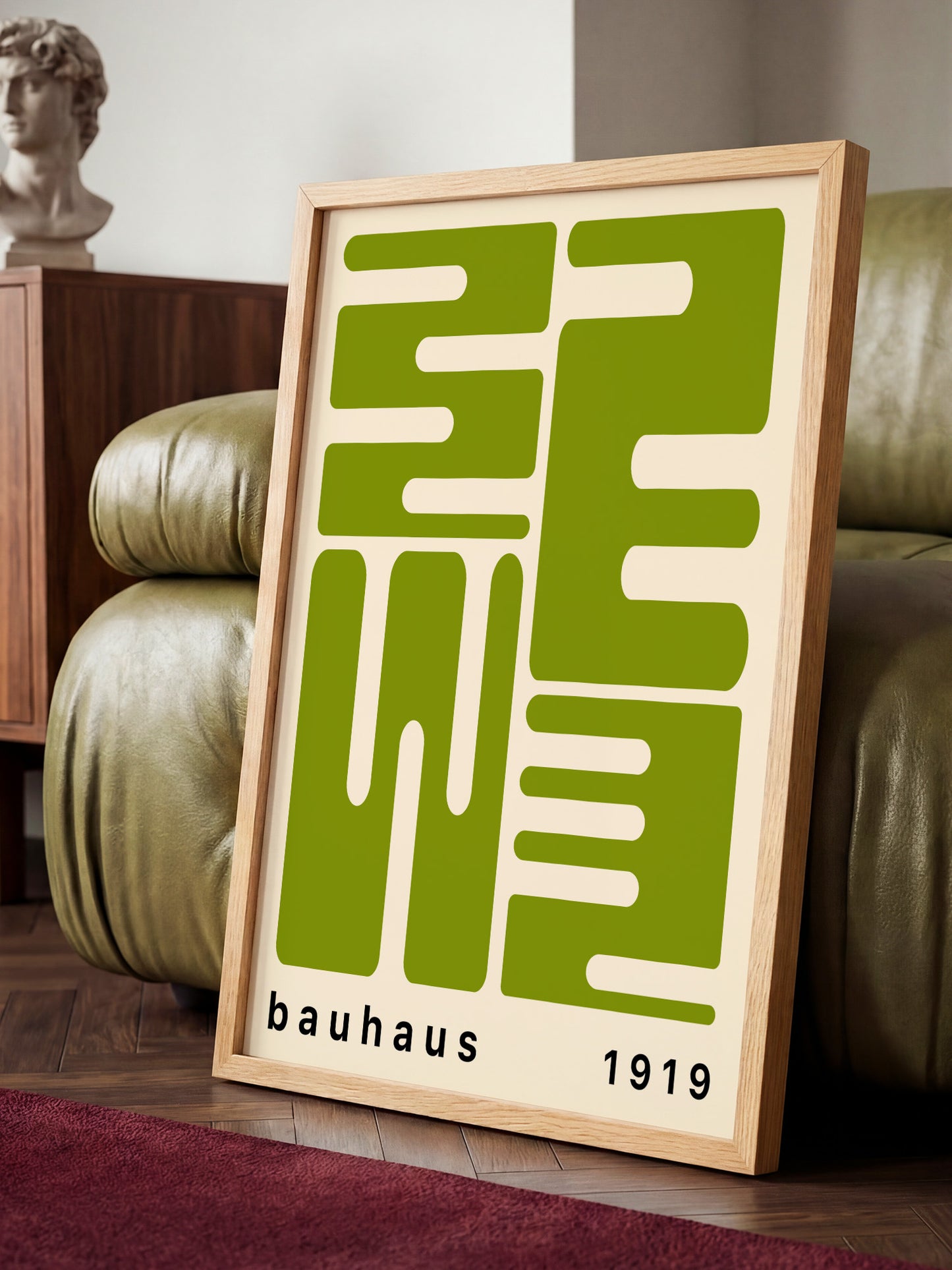 a framed poster with a large green geometric design and the text "bauhaus 1919" on it, placed on a wooden floor in front of a green leather couch.