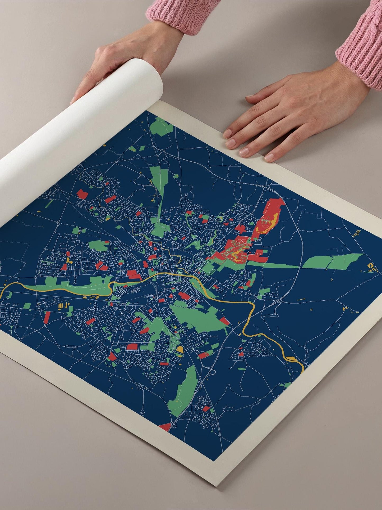 A person's hands are holding a roll of paper over a colorful map of a city, which appears to be a detailed and vibrant representation of the urban landscape.