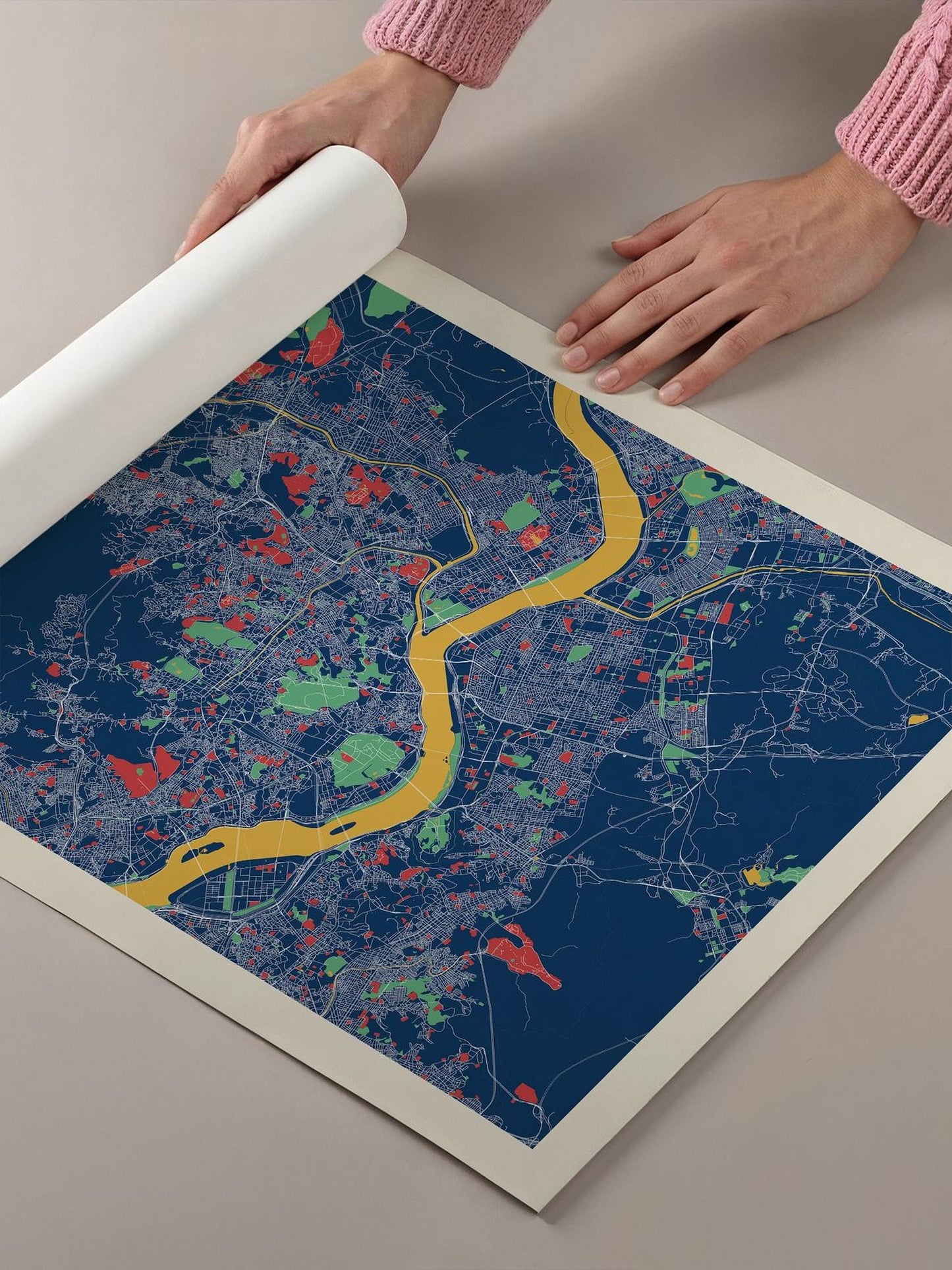 A person's hands are holding a roll of paper over a colorful map of a city, which appears to be a detailed and vibrant representation of the urban landscape.