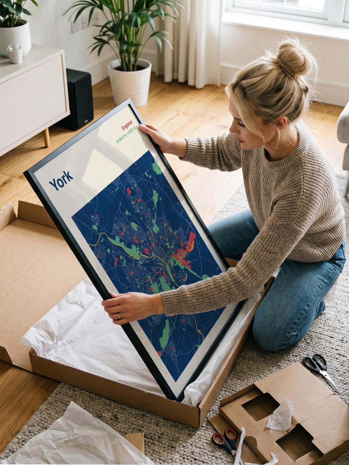 A woman is kneeling on the floor and holding a framed map of York, which is a city in England.