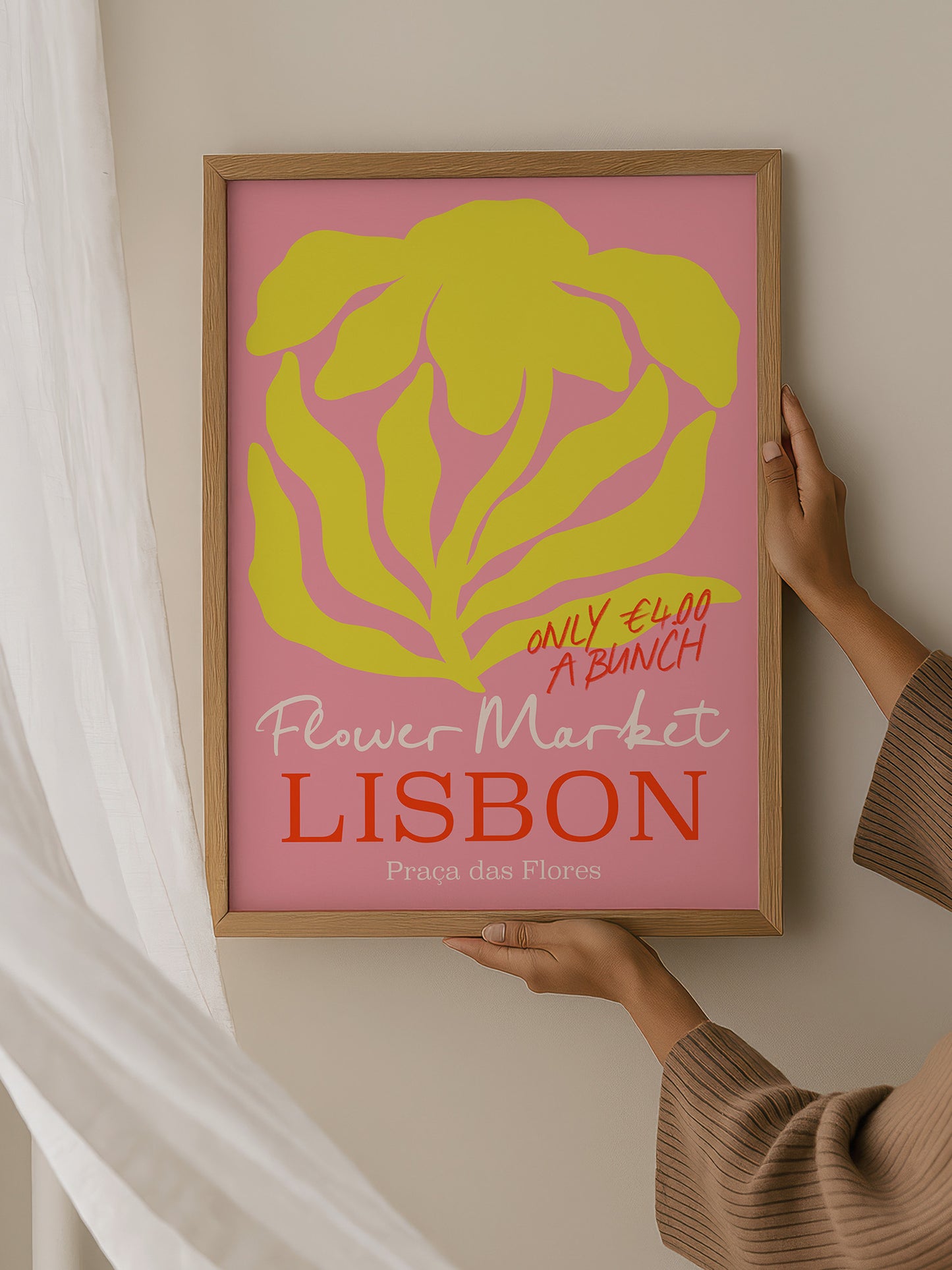 A person is holding up a framed poster advertising a flower market in Lisbon.