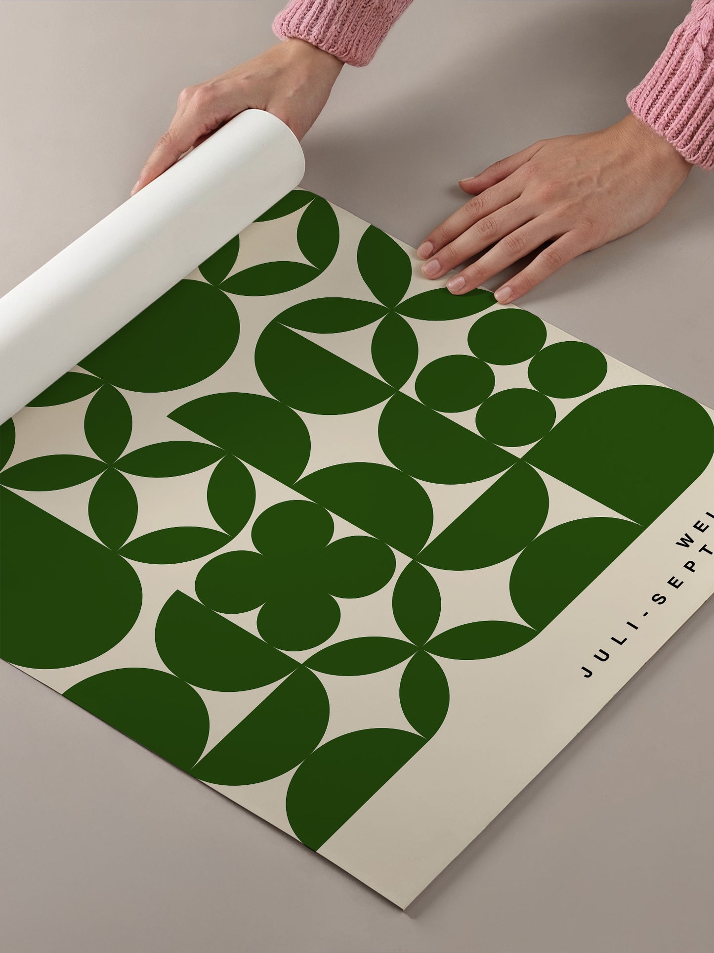 A person's hands are holding a roll of paper with a repeating pattern of green circles and white flowers on it.