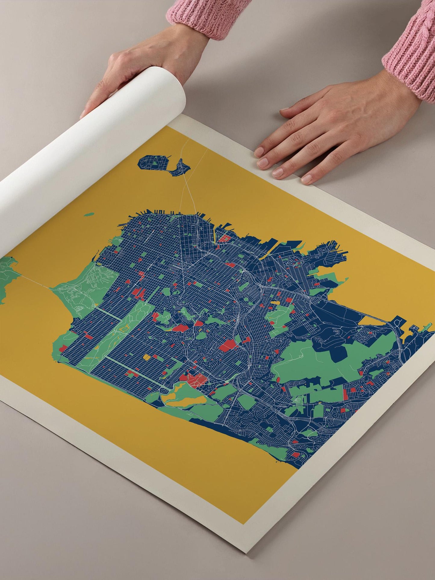 A person's hands are holding a roll of paper over a colorful map of a city, which appears to be a detailed and intricate illustration of the urban landscape.