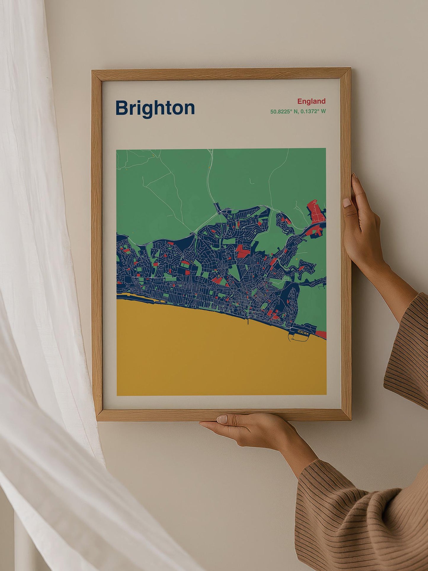 A person is holding up a framed map of Brighton, England, which features a colorful and detailed representation of the city.