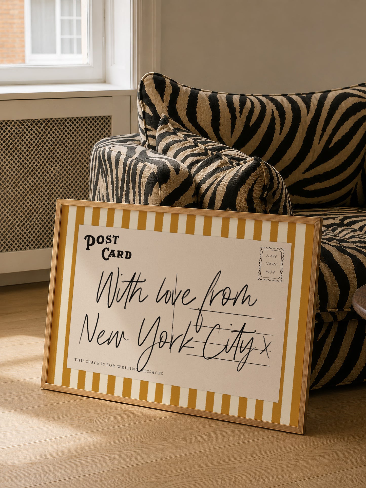A framed postcard with handwritten text is placed on a couch in a room with a window.