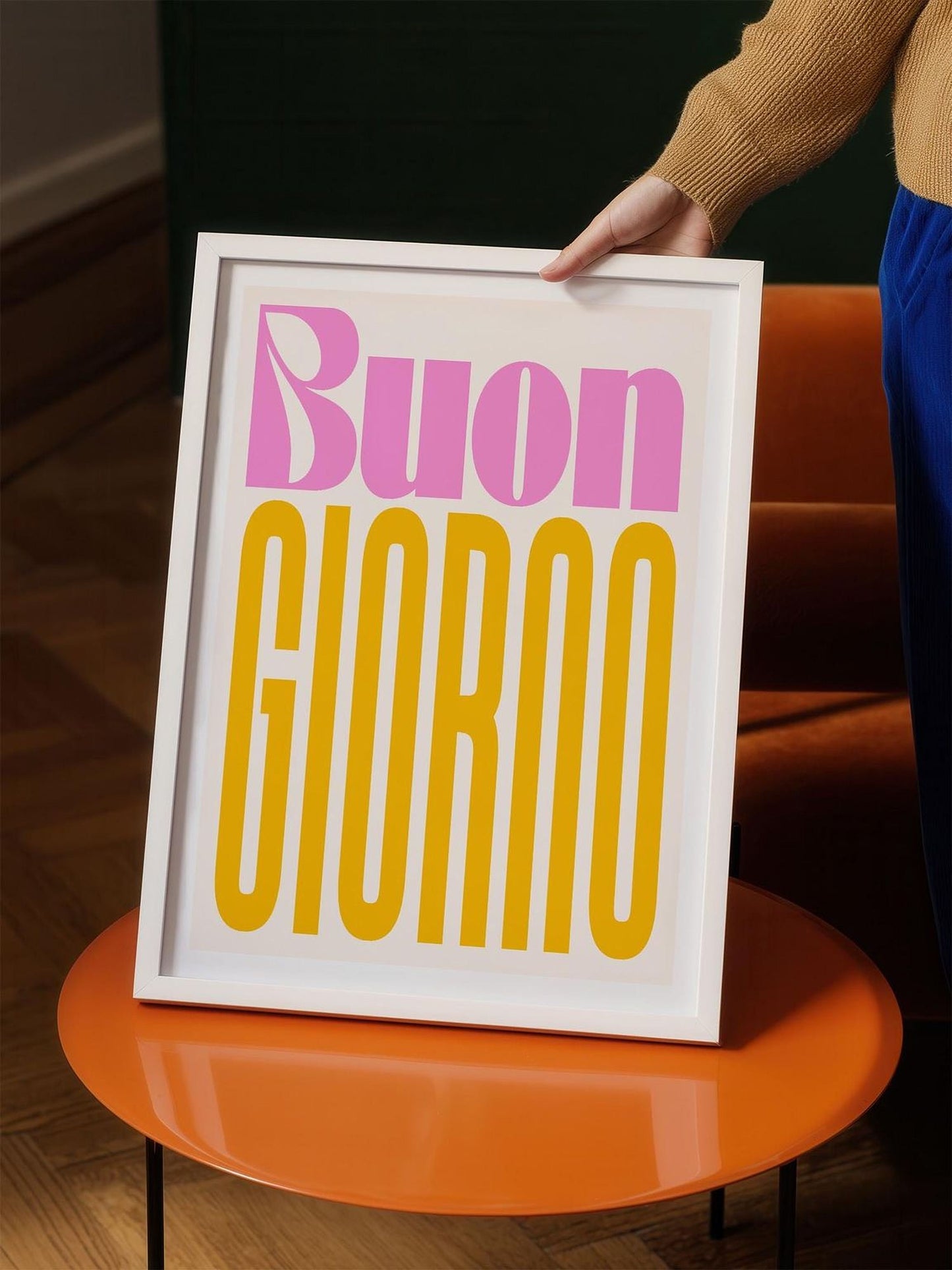 A person is holding up a framed poster with the text "Buon Giorno" in a white frame.