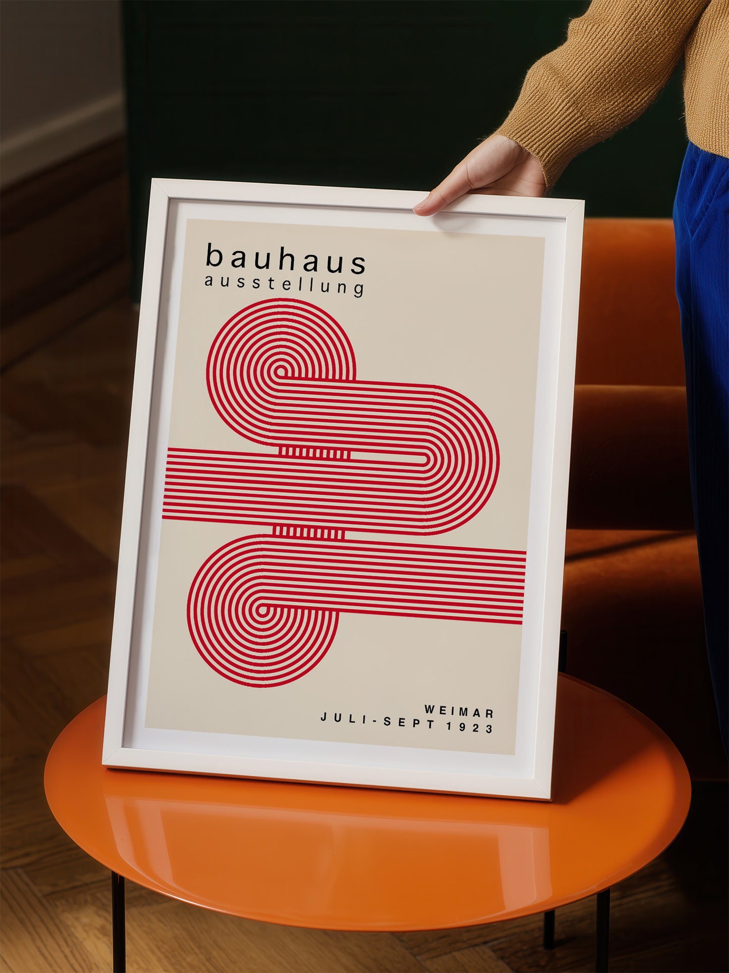 A person is holding a framed poster with a minimalist design featuring a red and white spiral pattern.