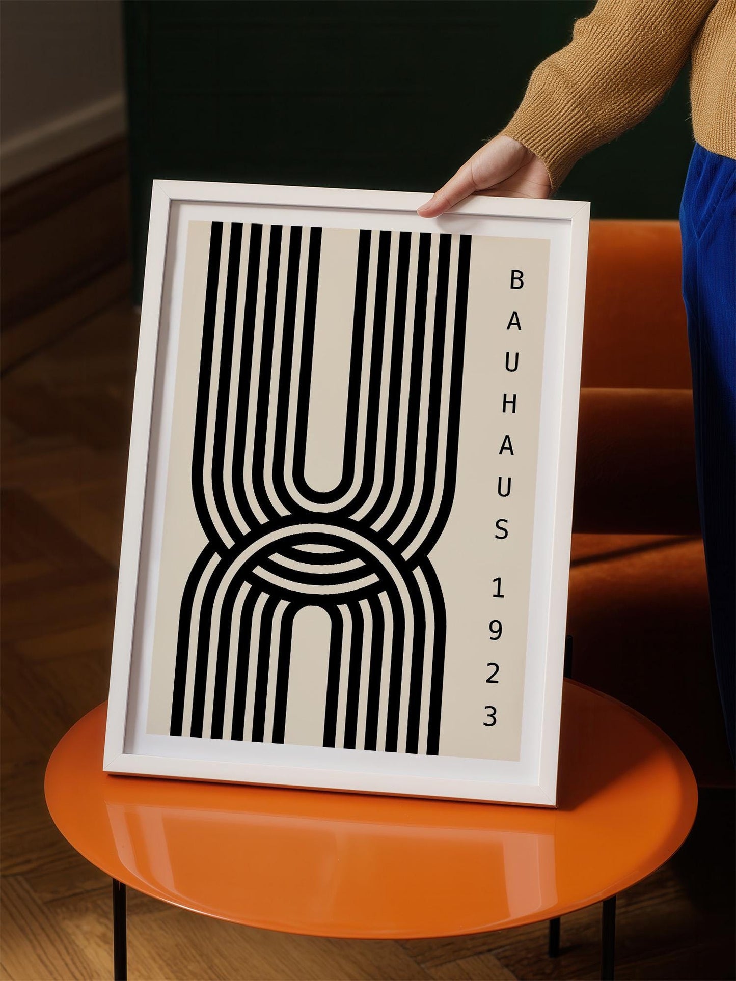 A person is holding a framed poster with a minimalist design featuring a large black and white line pattern.