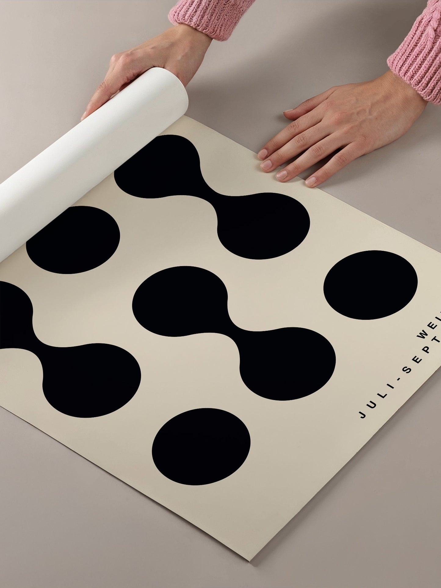 A person's hands are holding a roll of paper with a black and white geometric pattern on it.