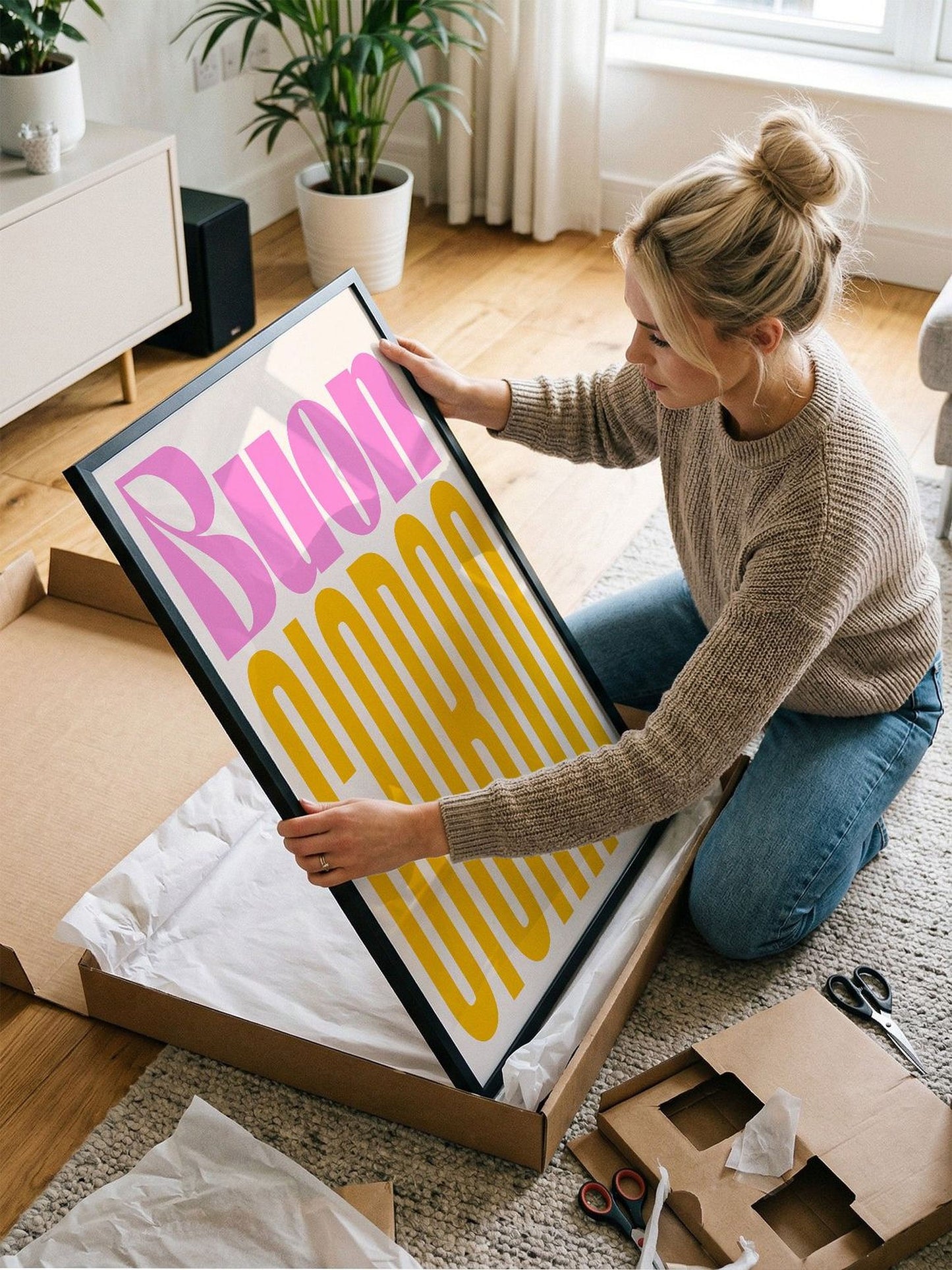 A woman is kneeling on the floor and holding a large framed poster with the word "Buon" written on it.