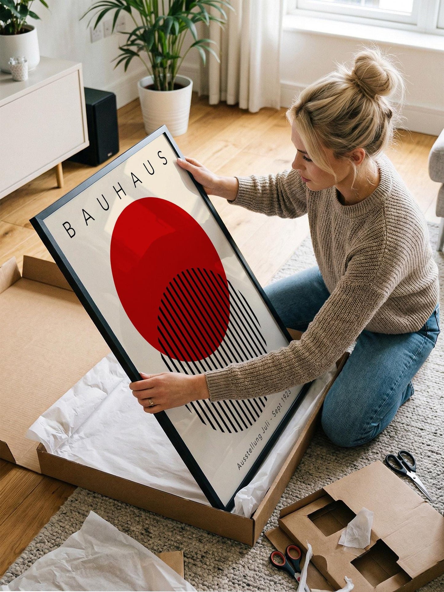 A woman is kneeling on the floor and holding a framed poster with a red circle and black stripes.