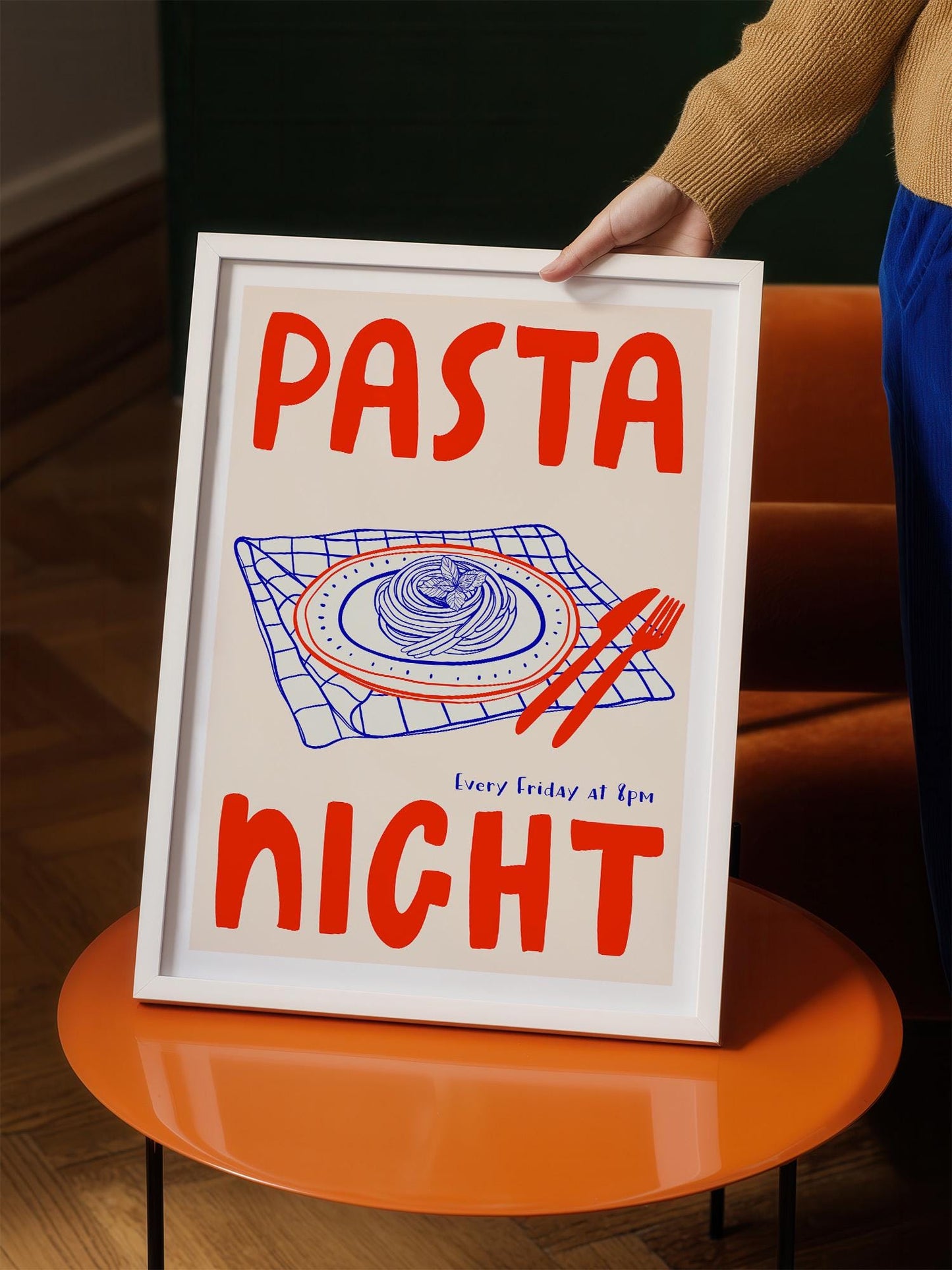 A person is holding up a framed poster with the text "PASTA NIGHT" and an illustration of a plate of pasta.