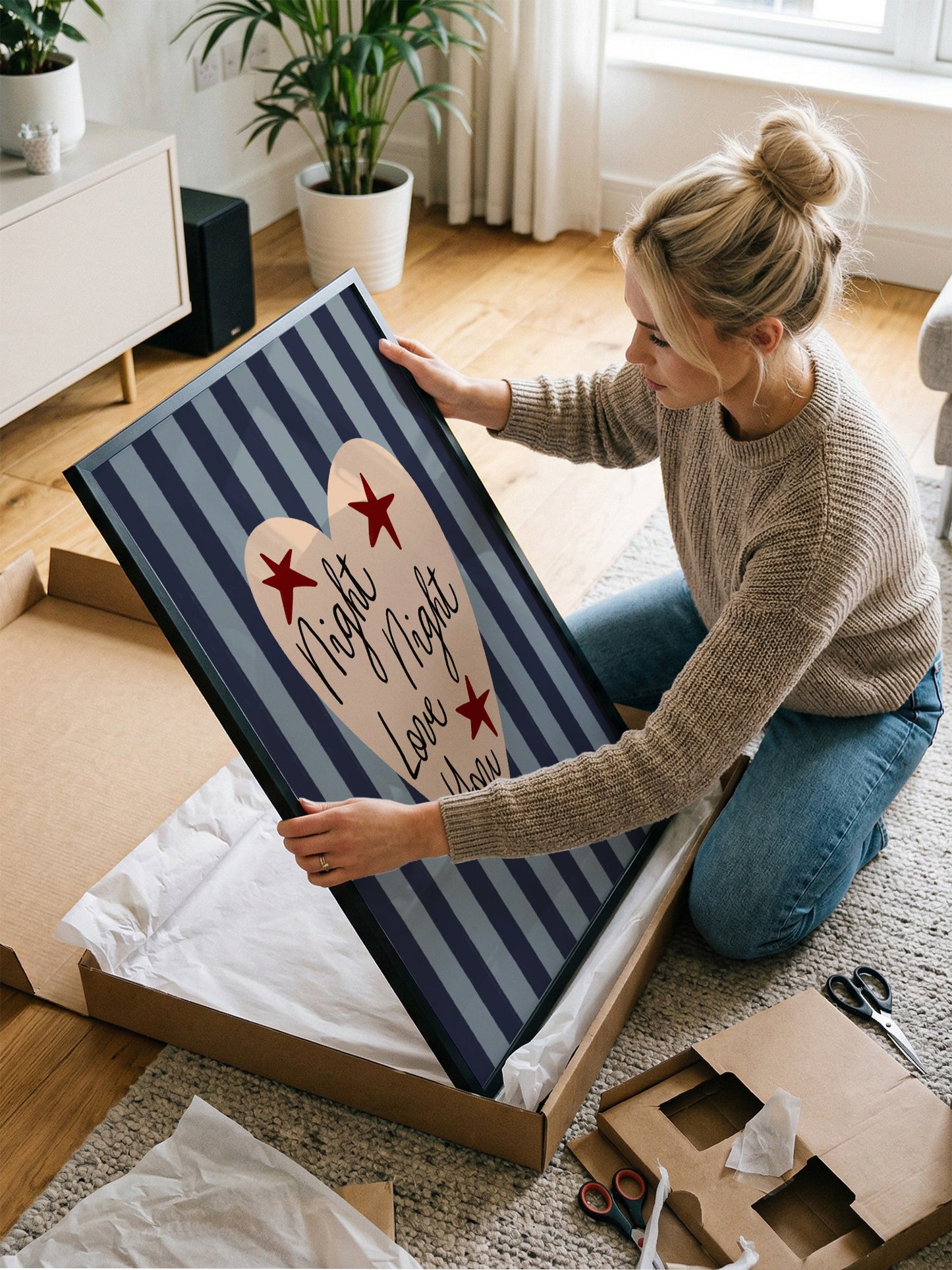 A woman is kneeling on the floor and holding a large framed picture with a heart design.