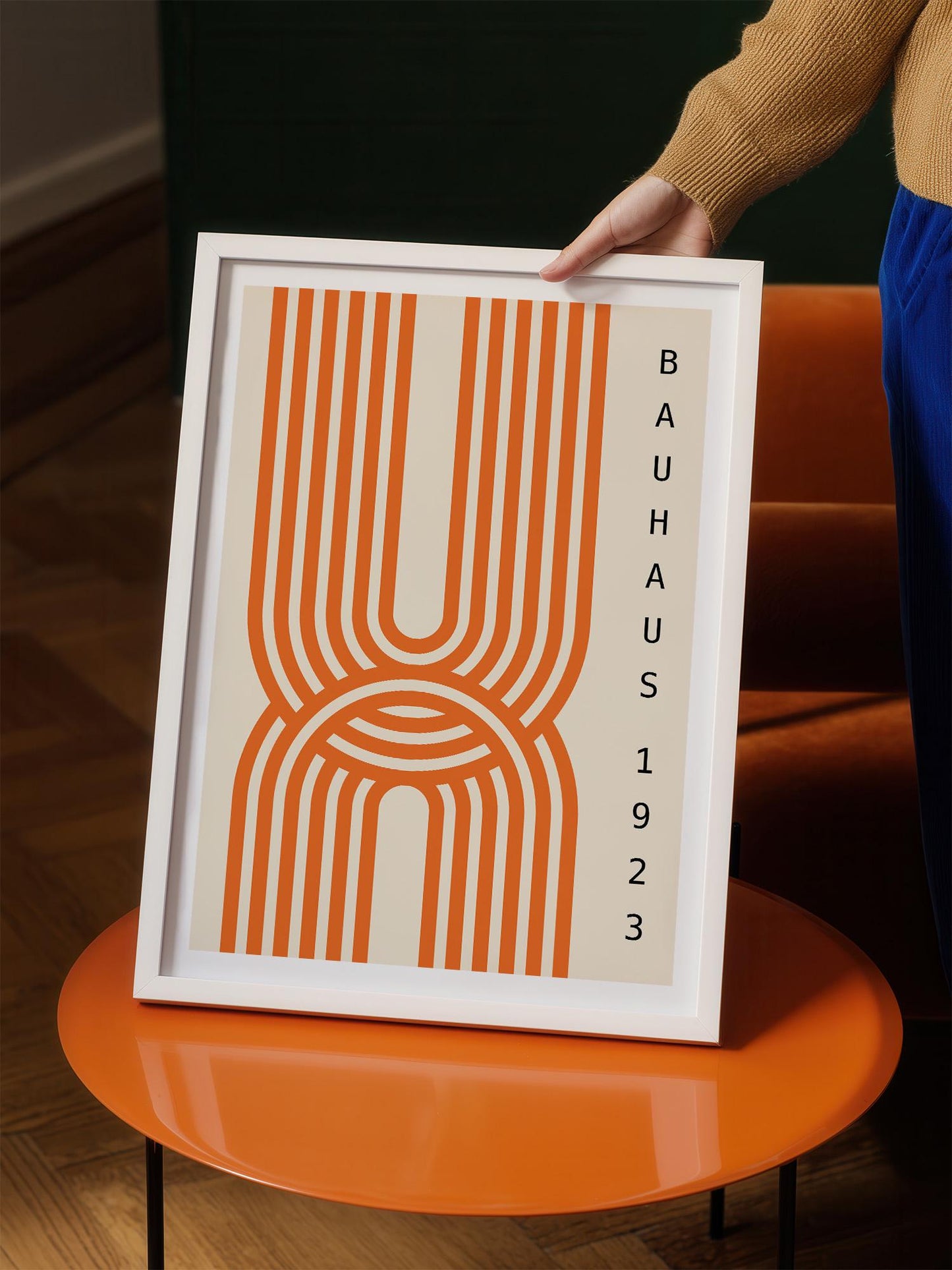 A person is holding a framed poster with an abstract design featuring orange and white stripes.