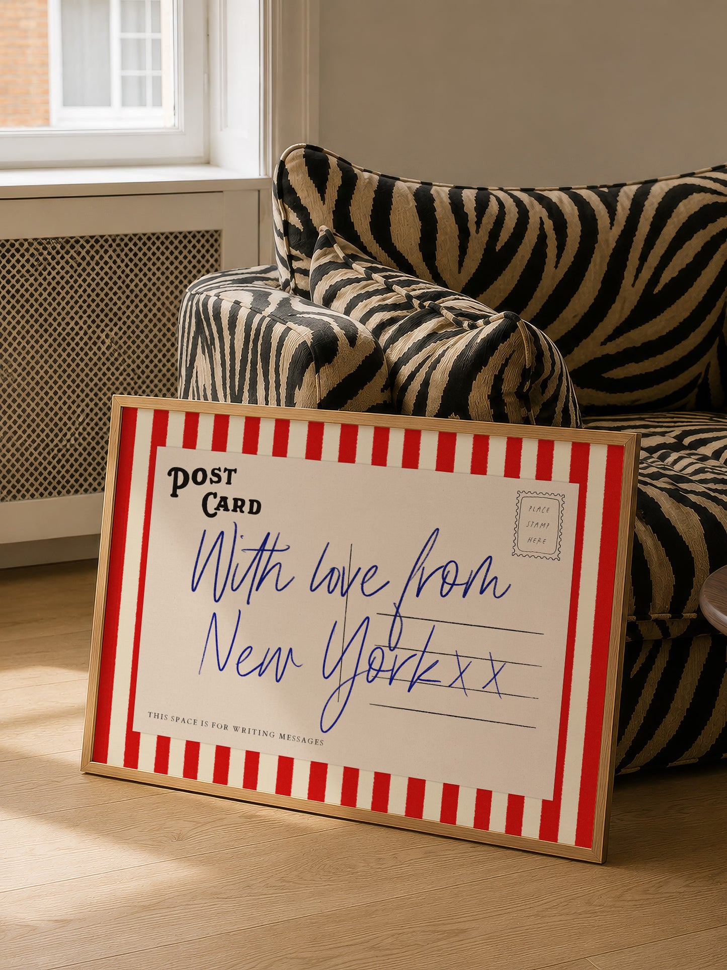 A framed postcard with a handwritten message is placed on a couch in a room.