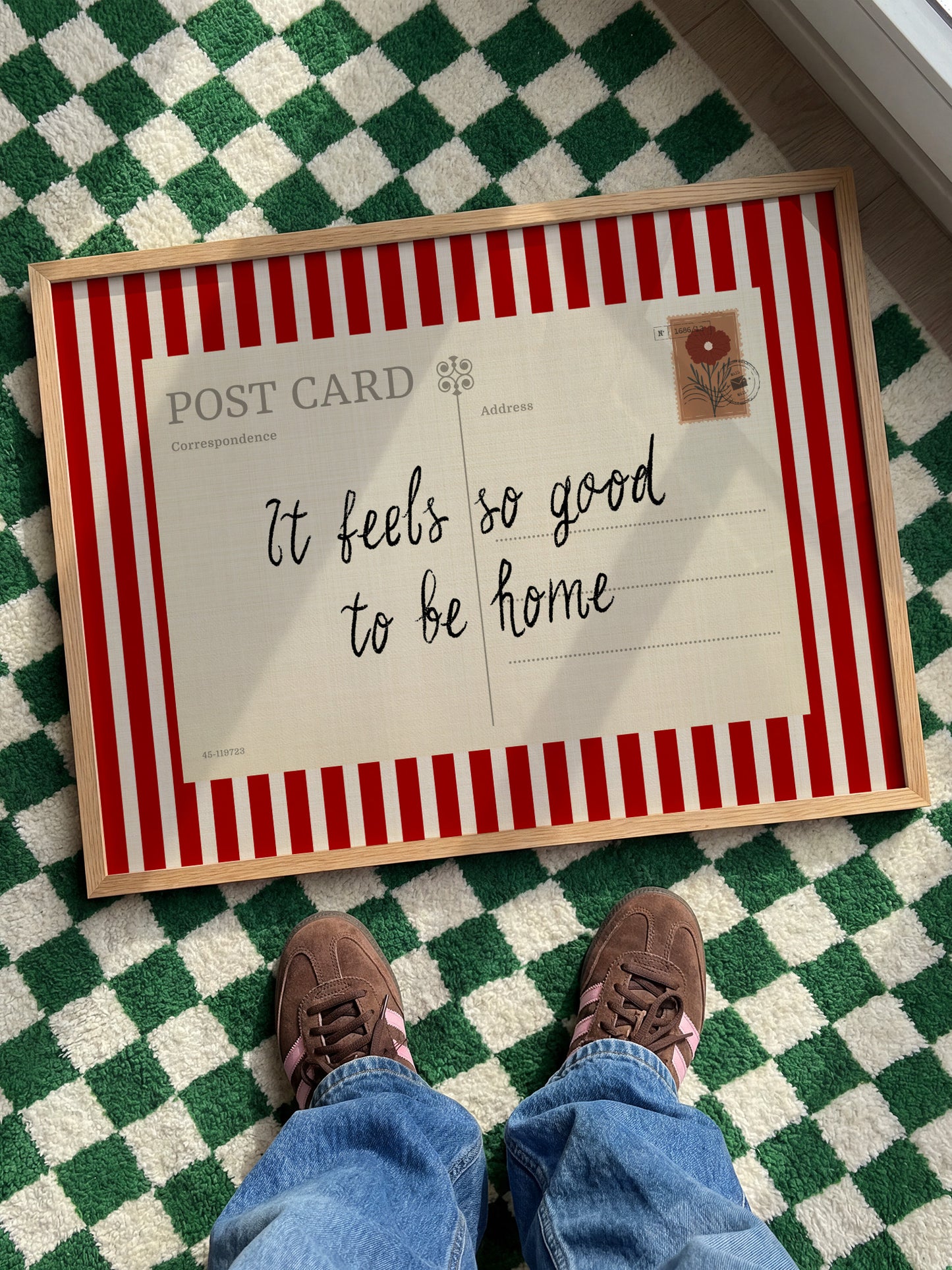 A person's feet are positioned in front of a framed postcard with a handwritten message that reads "It feels so good to be home".