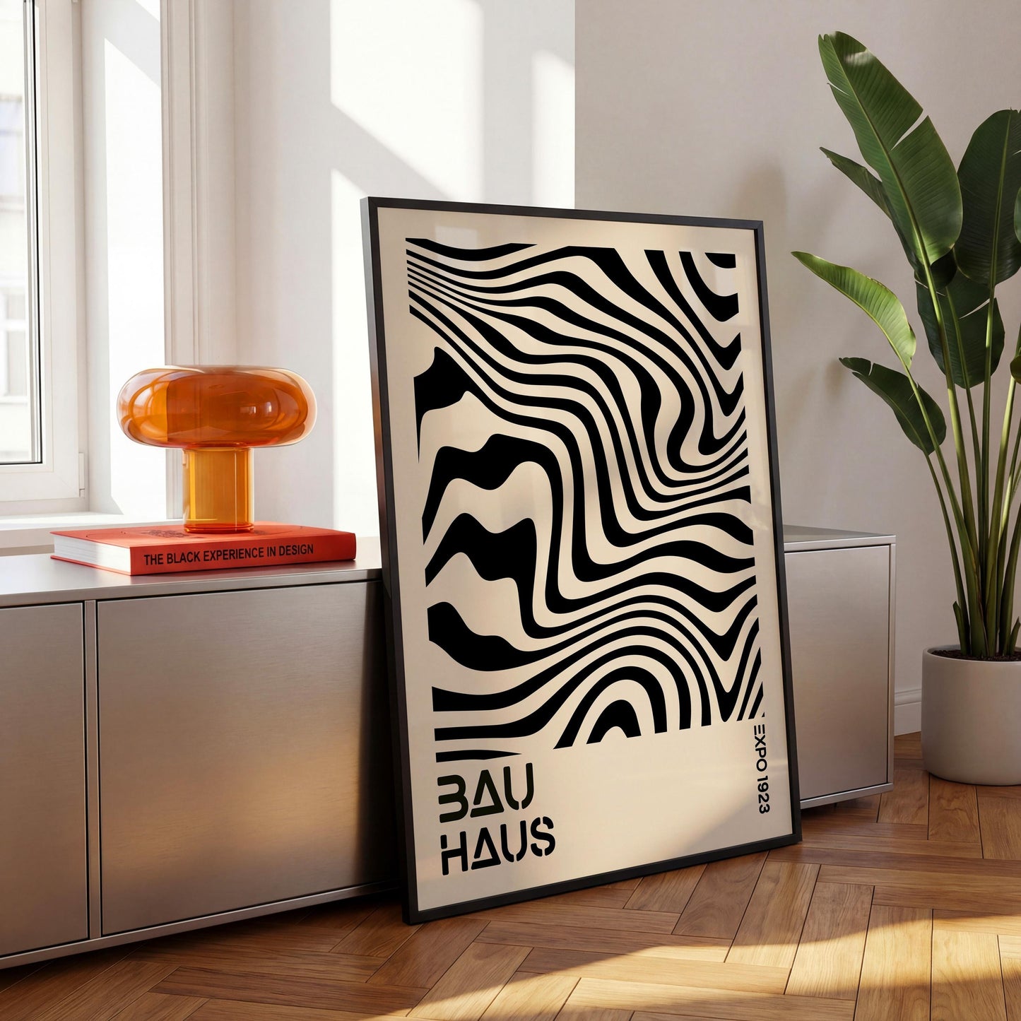 a minimalist black and white abstract art poster with the text "BAU HAUS" on it, placed on a wooden floor next to a potted plant and a small orange lamp.