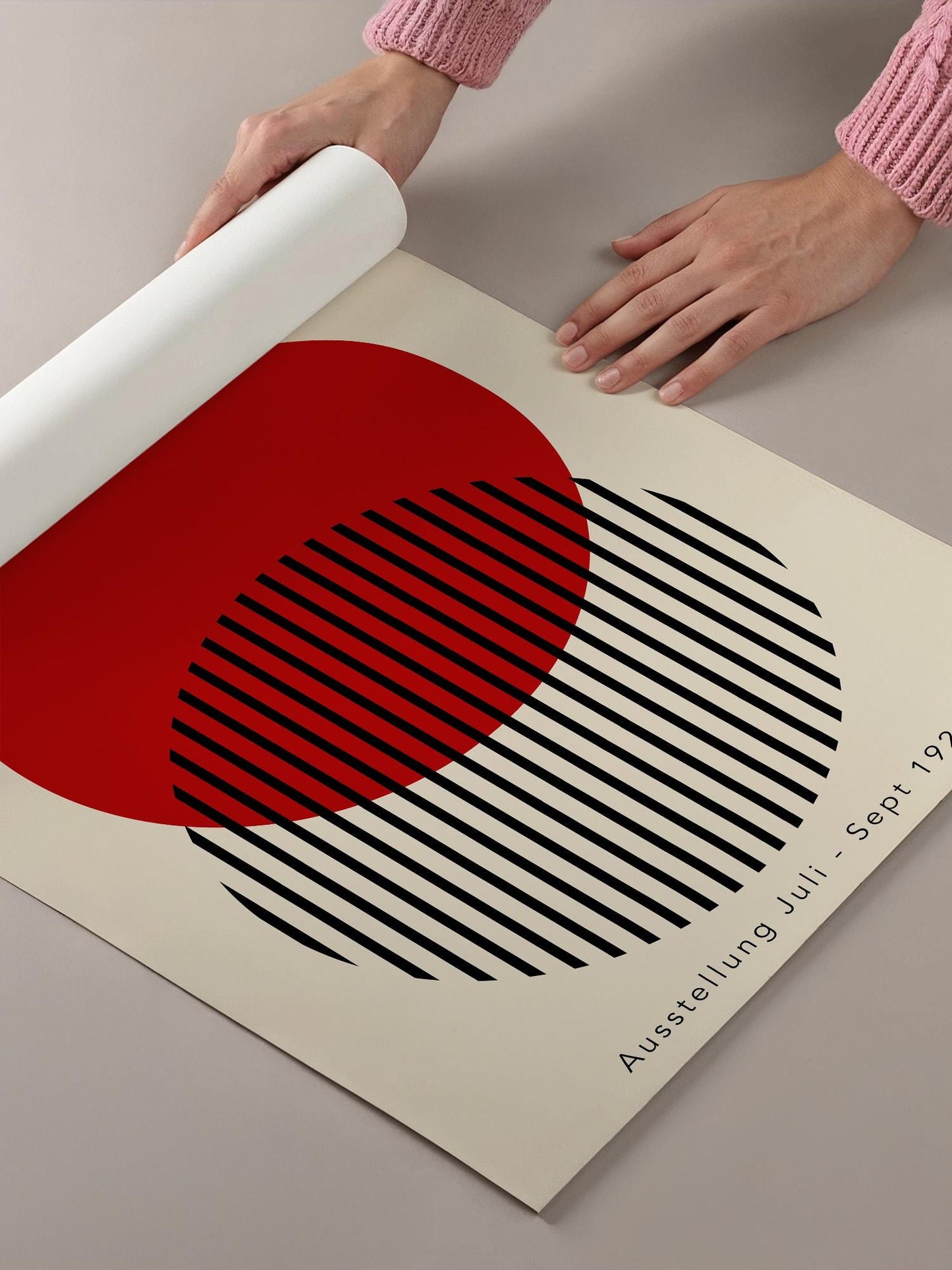 A person's hands are holding a roll of paper, which appears to be a poster or artwork with a striking design featuring a red circle and black stripes.