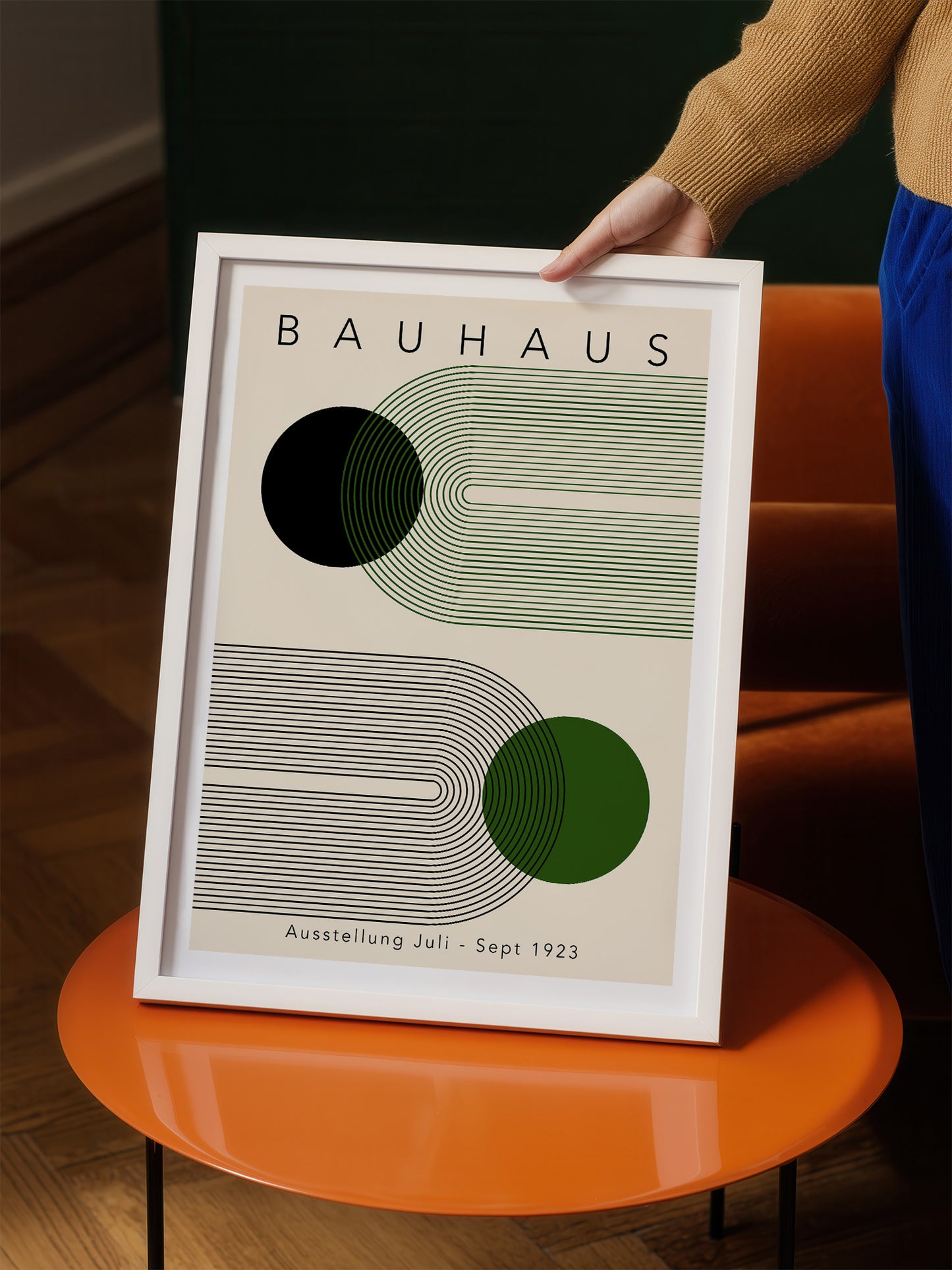 A person is holding up a framed poster of the Bauhaus art school, featuring abstract geometric designs in shades of green and black.
