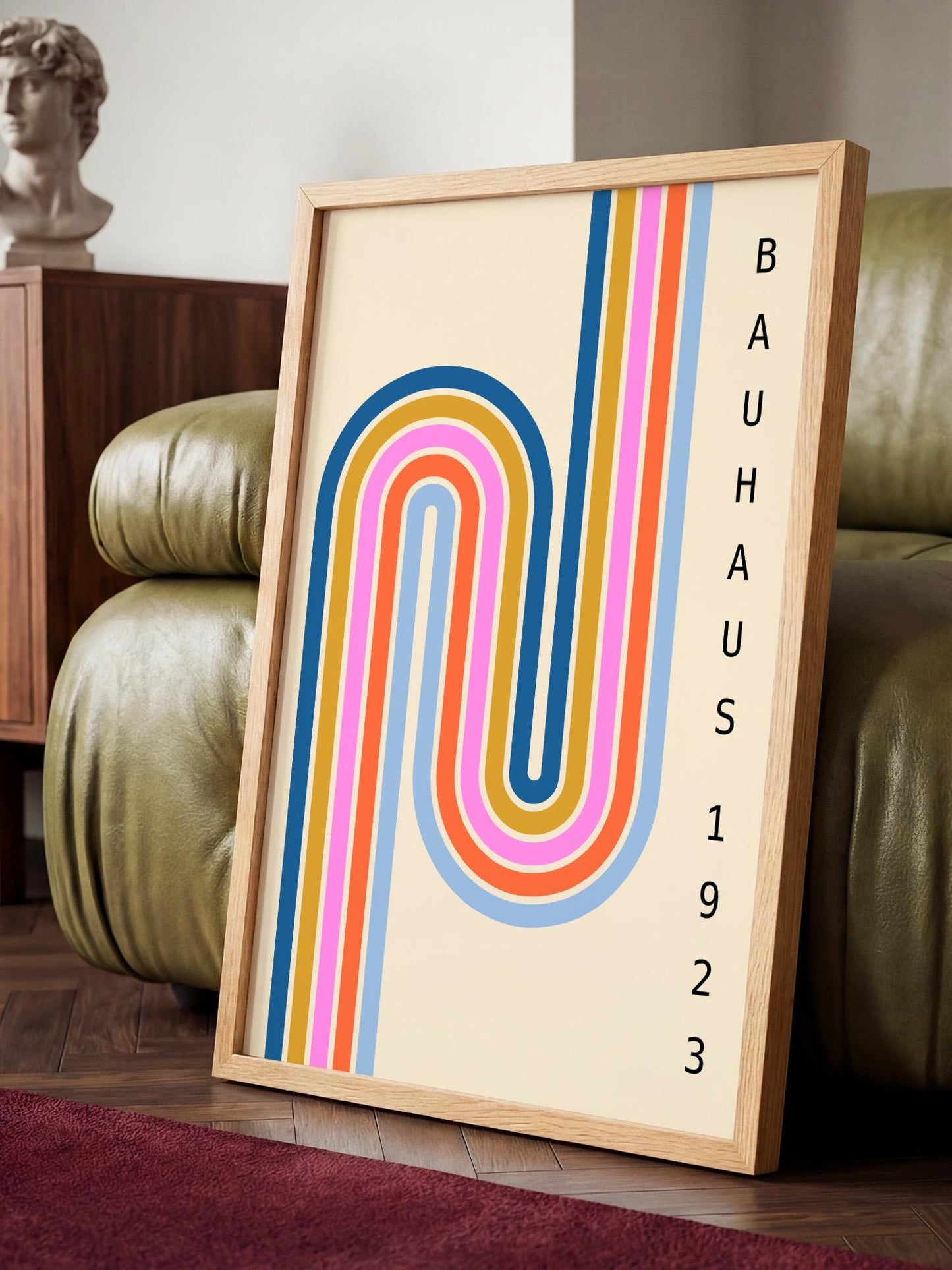 A framed poster with a colorful abstract design featuring a curved line pattern in various colors, including pink, blue, orange, and yellow. The poster is displayed on a wooden stand in a room with a green leather couch.