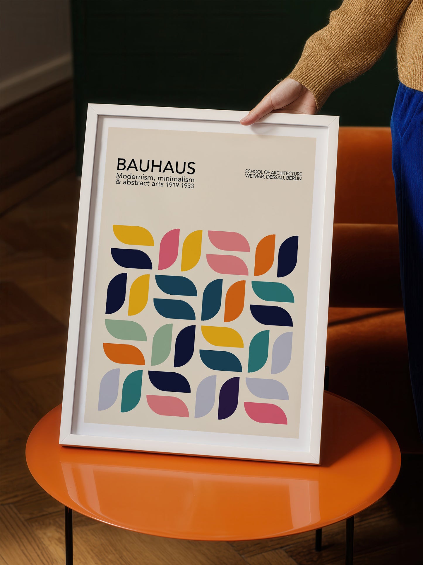 A person is holding a framed poster of the Bauhaus art school, featuring a geometric design with various shapes and colors.