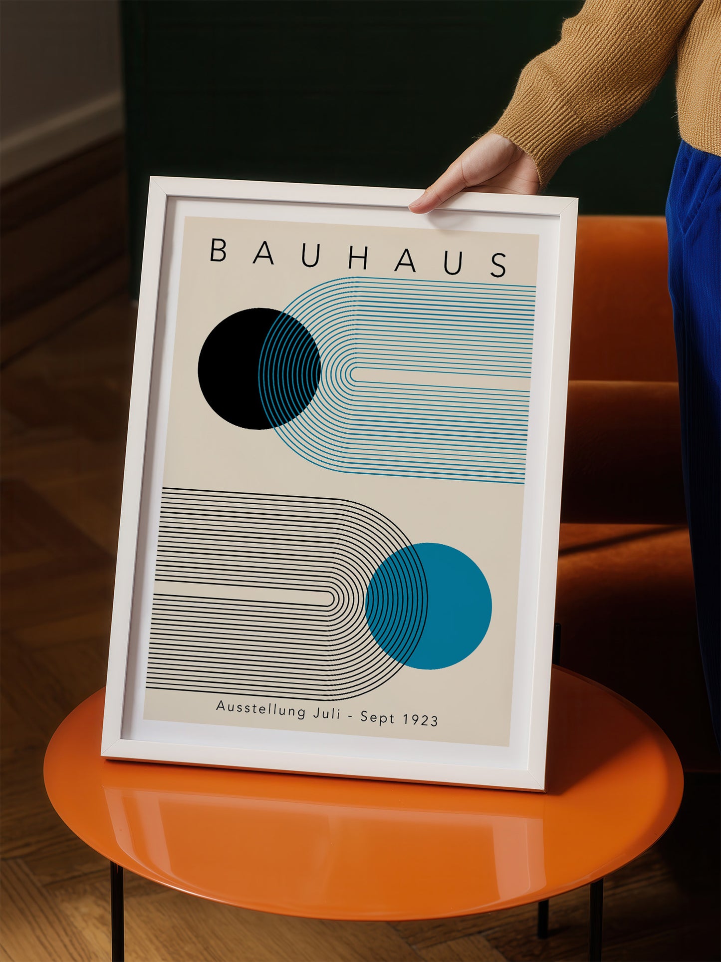 A person is holding a framed poster of the Bauhaus art school, featuring abstract geometric designs in shades of blue and gray.