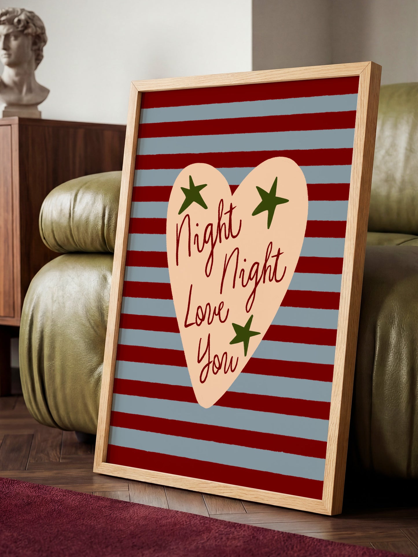 A framed poster with a heart-shaped design and the text "Night, Night, Love You" is displayed on a wooden floor in a room with a green couch.