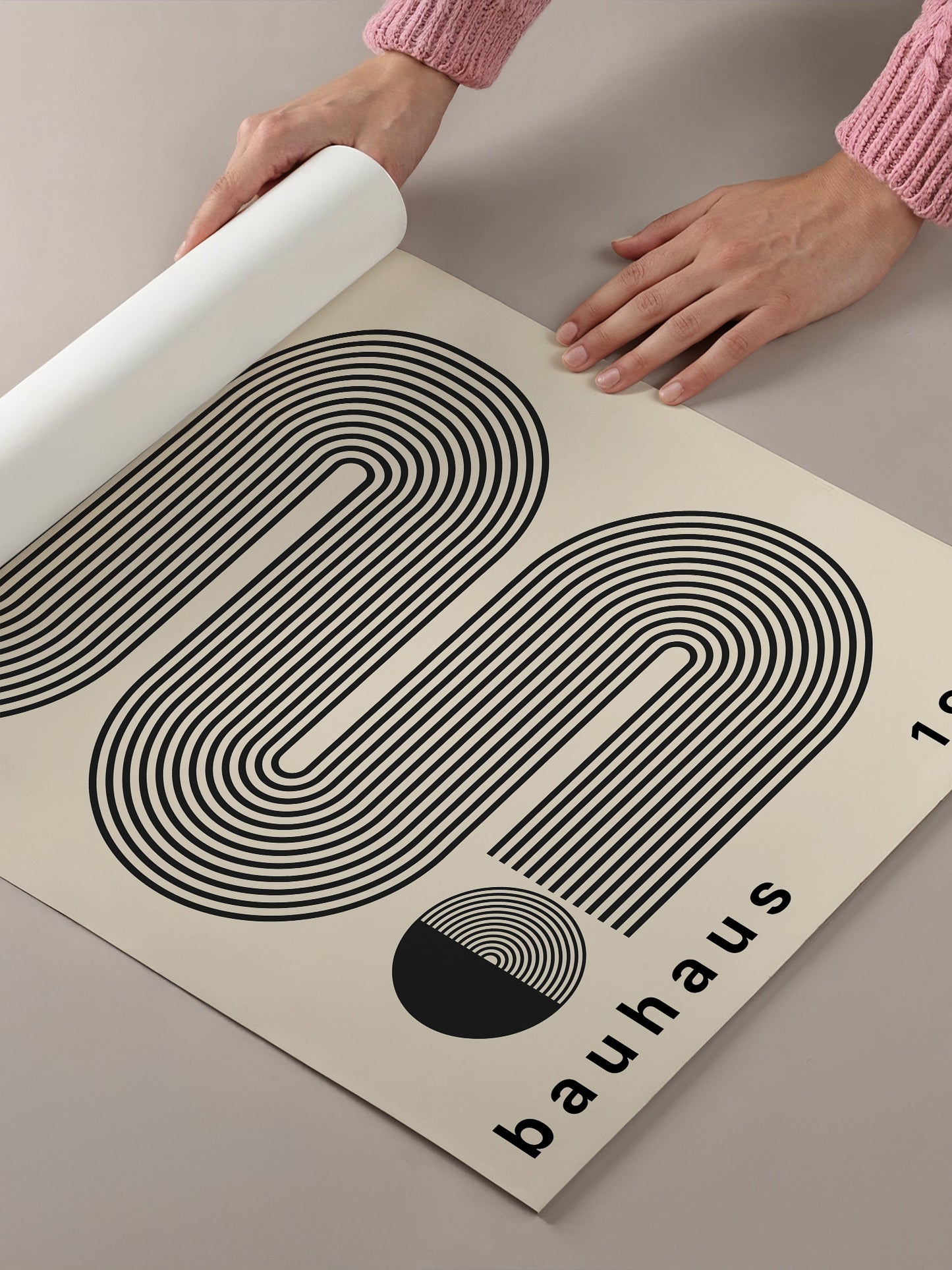 A person's hands are holding a roll of paper, which appears to be a poster or artwork featuring a black and white abstract design with curved lines and a circular element.