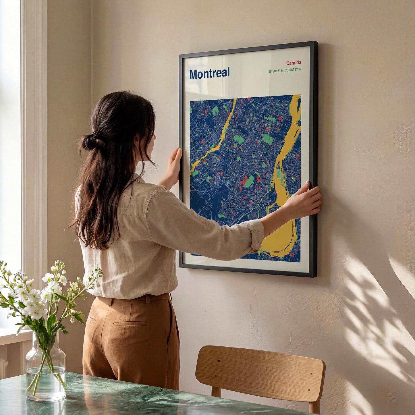 A woman is hanging a framed map of Montreal on a wall.