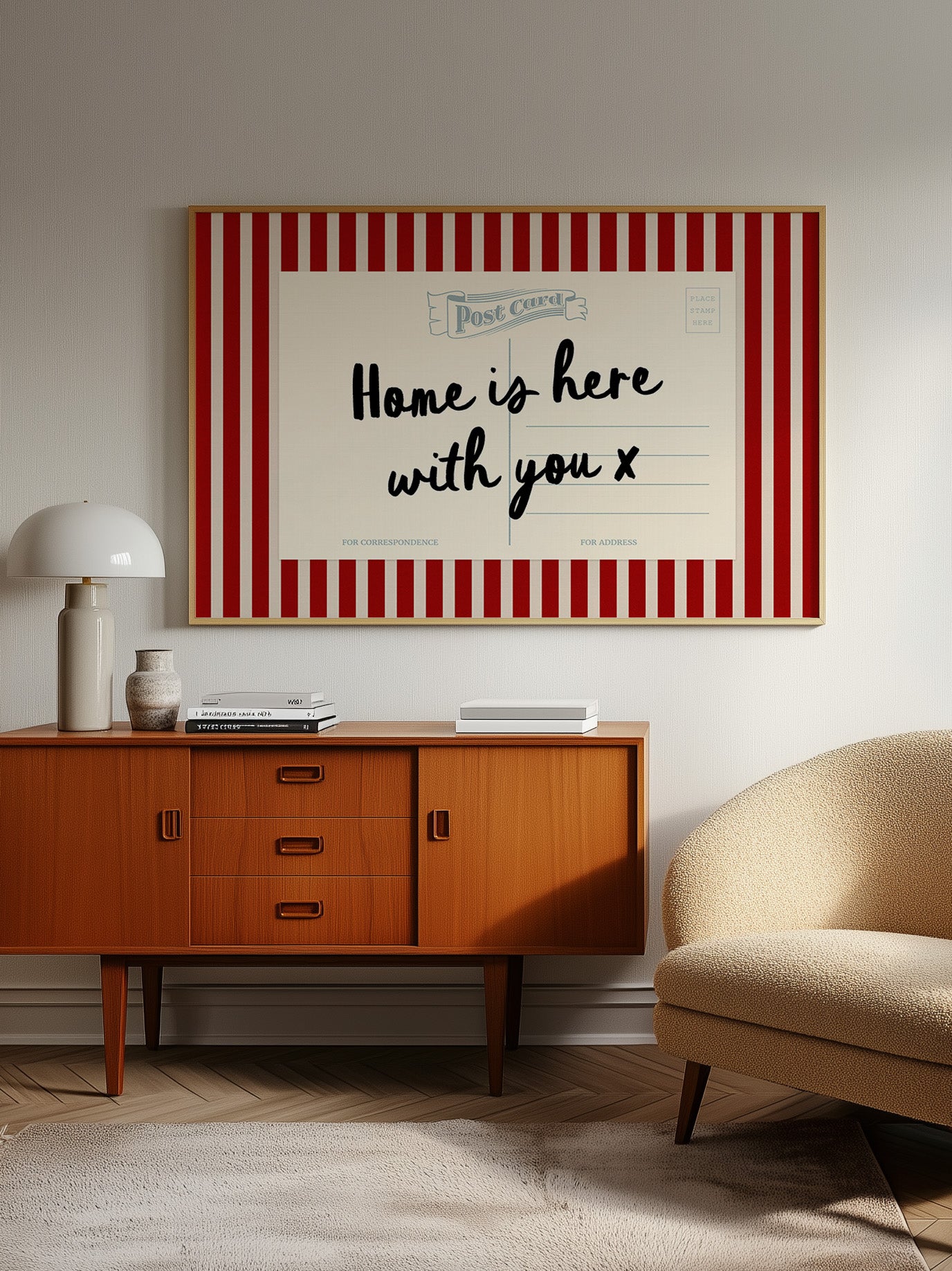 a vintage-style wooden cabinet with a red and white striped border, a lamp, a beige armchair, and a framed poster with the text "Home is here with you x" on the wall.
