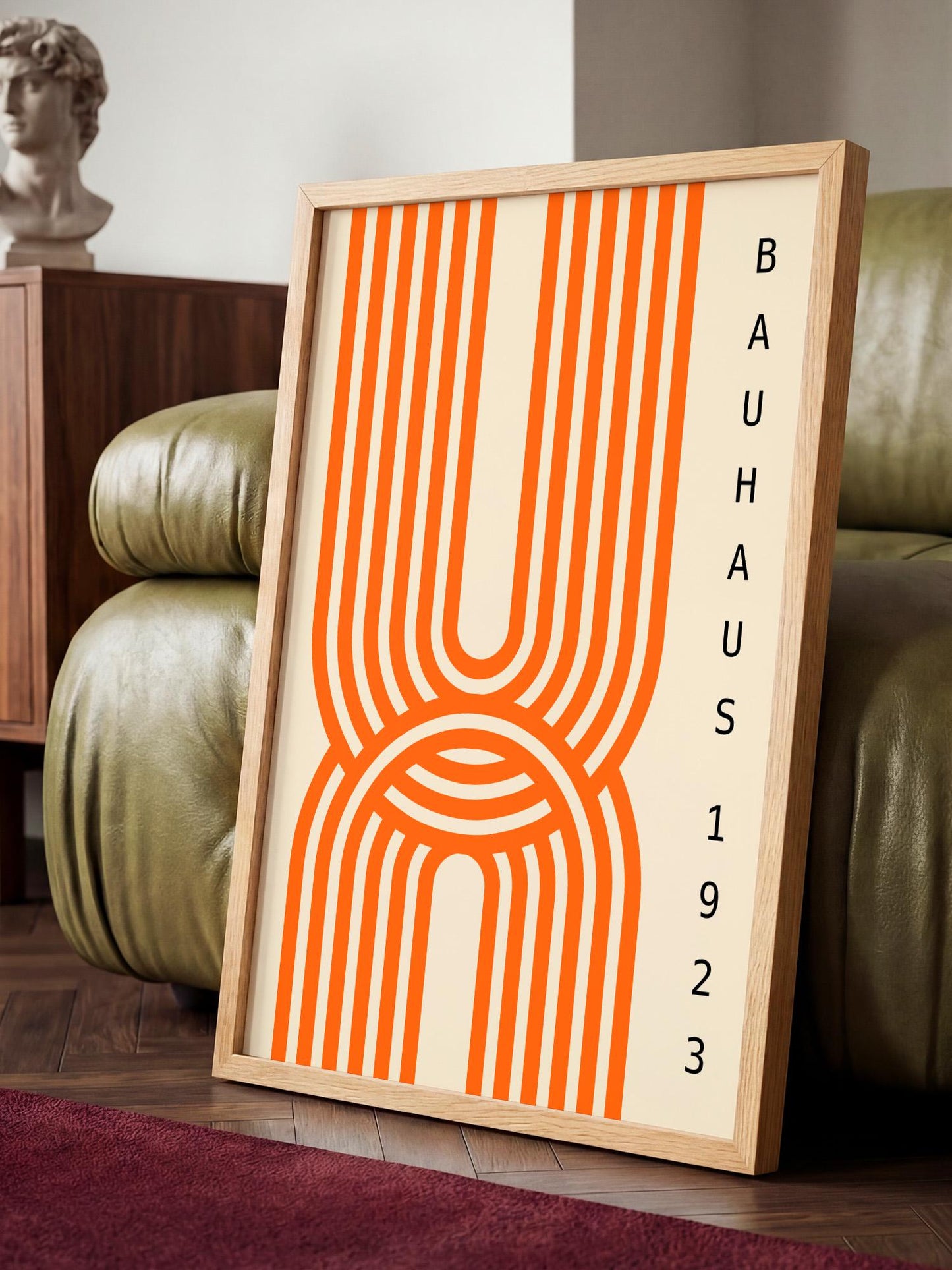 a framed poster with a striking orange and white abstract design, placed on a wooden floor in a room with a green leather couch.