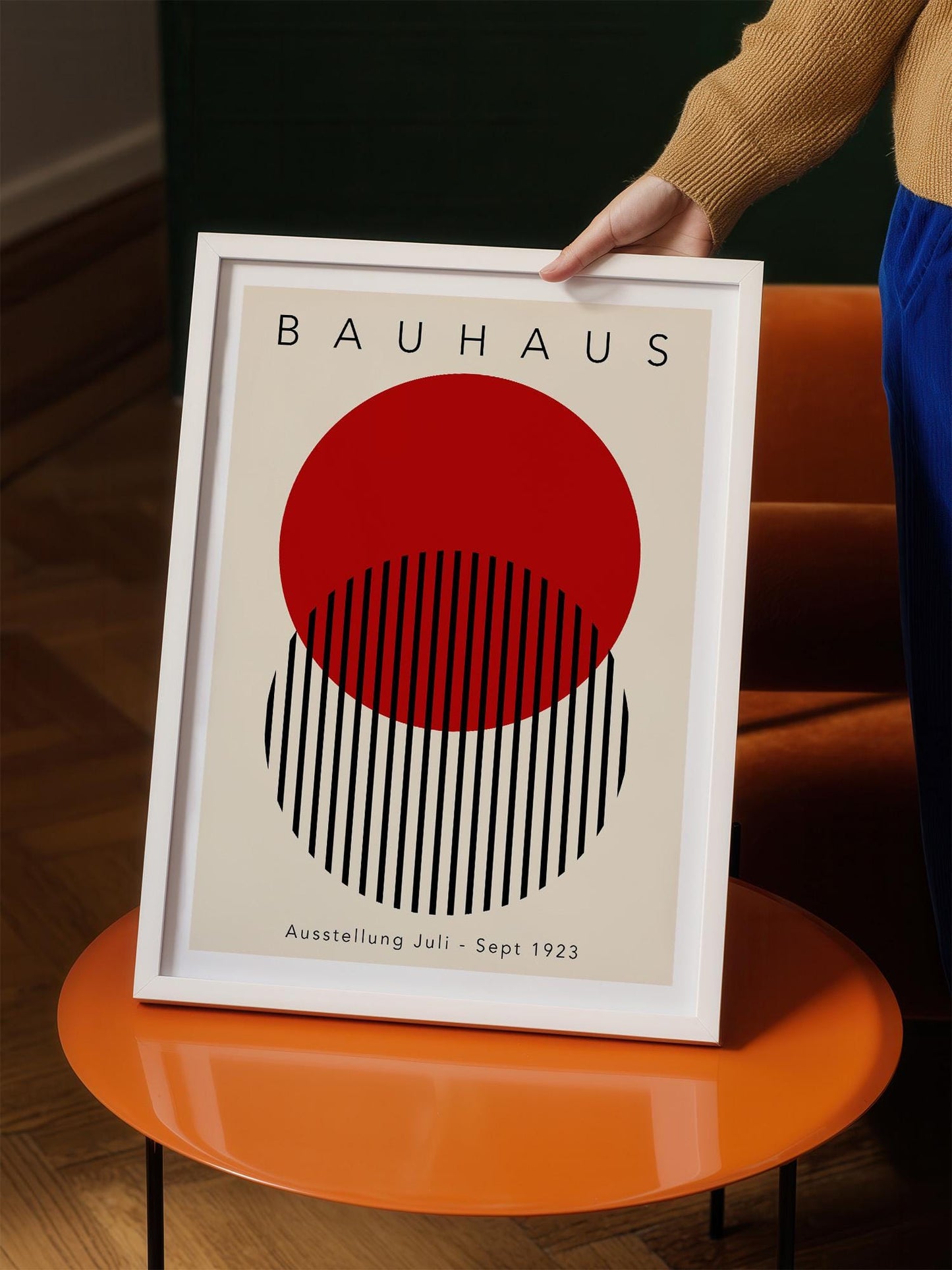 A person is holding up a framed poster of the Bauhaus art movement, featuring a bold red circle and black stripes.