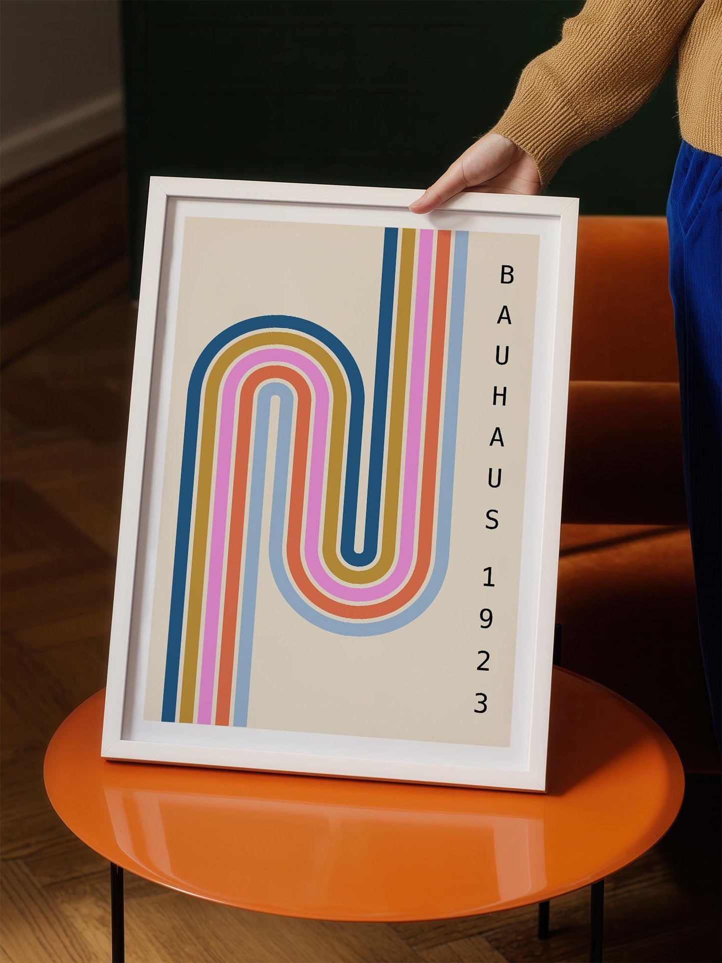 A person is holding a framed poster with a colorful abstract design featuring a curved line pattern in various colors.