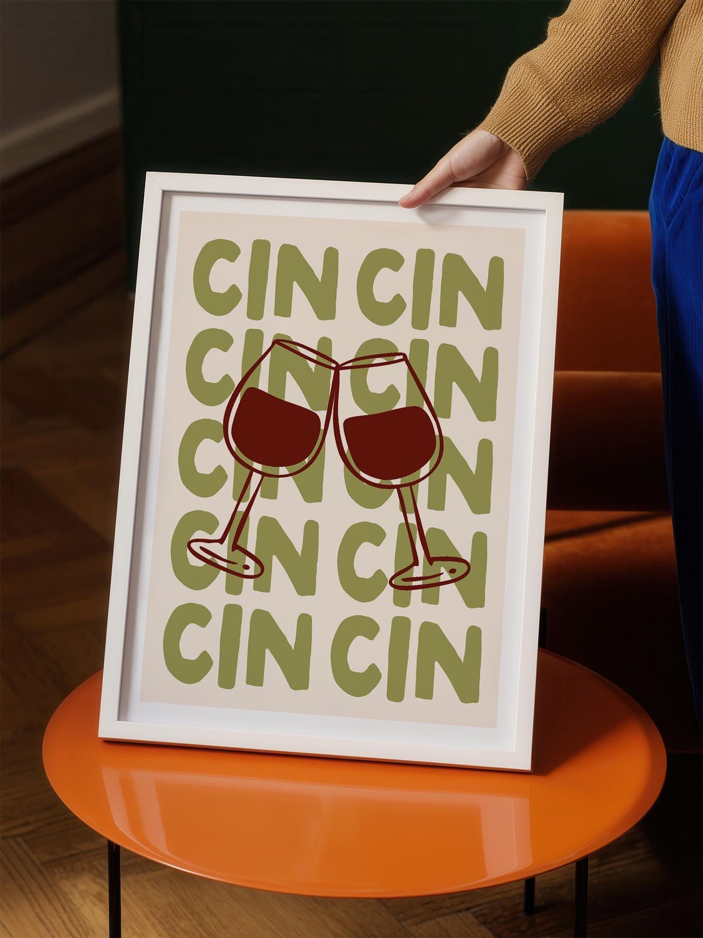 A person is holding up a framed print with a graphic design featuring two wine glasses with the word "CINCI" repeated across them.