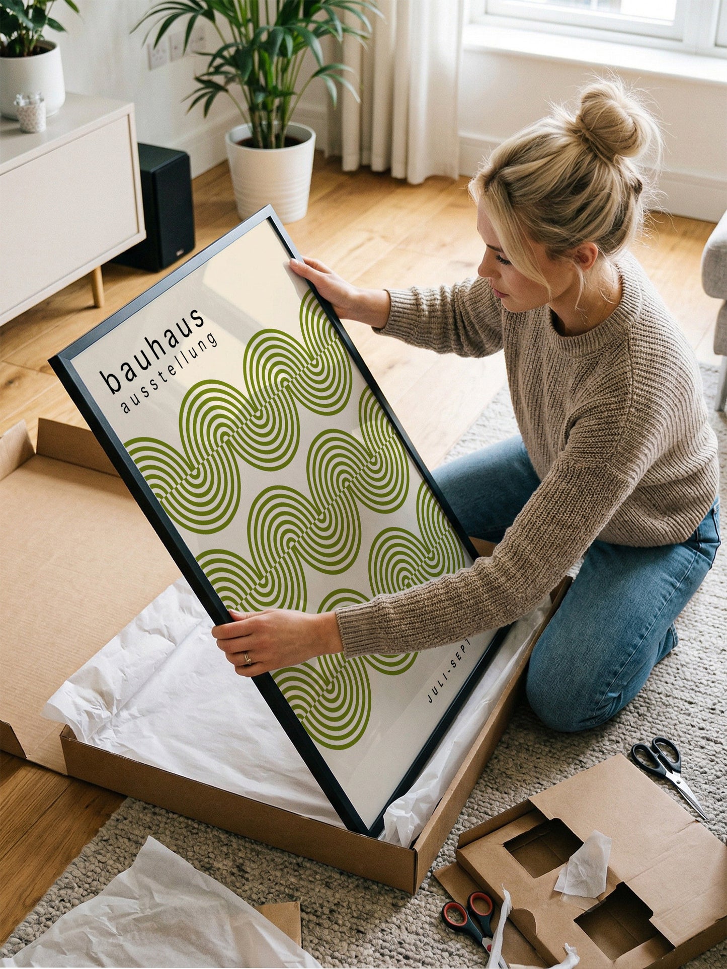 A woman is kneeling on the floor and holding a framed poster with a green and white spiral design.