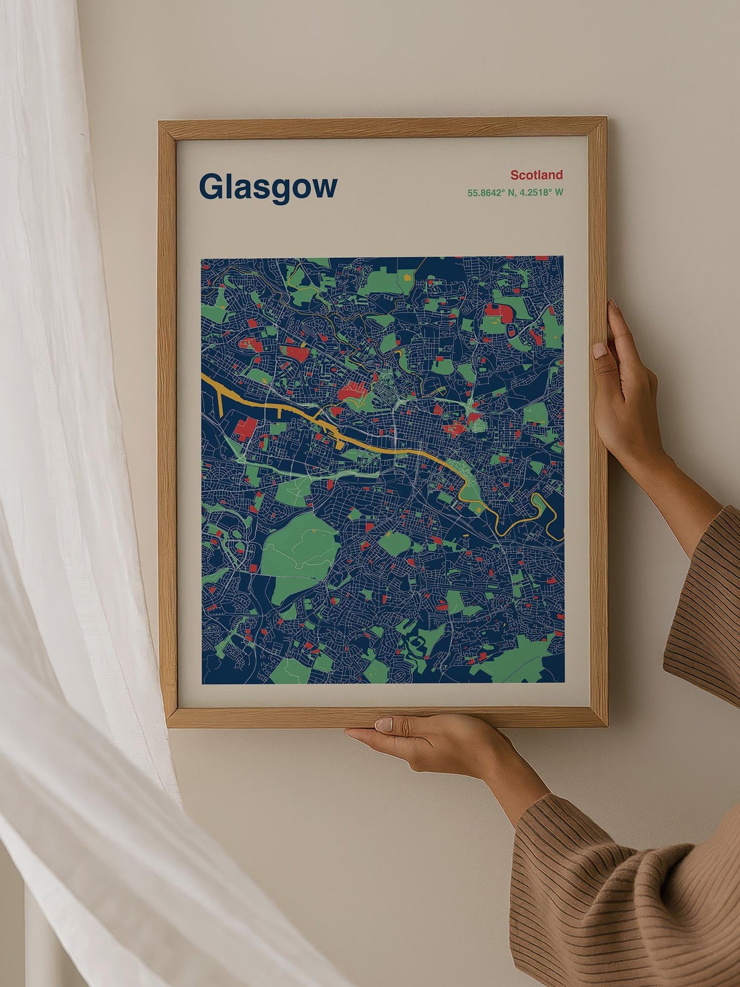 A person is holding up a framed map of Glasgow, Scotland, which is a colorful and detailed representation of the city.