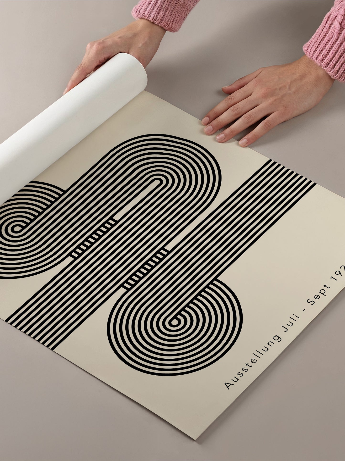 A person's hands are holding a roll of paper with a black and white abstract design featuring curved lines and shapes.