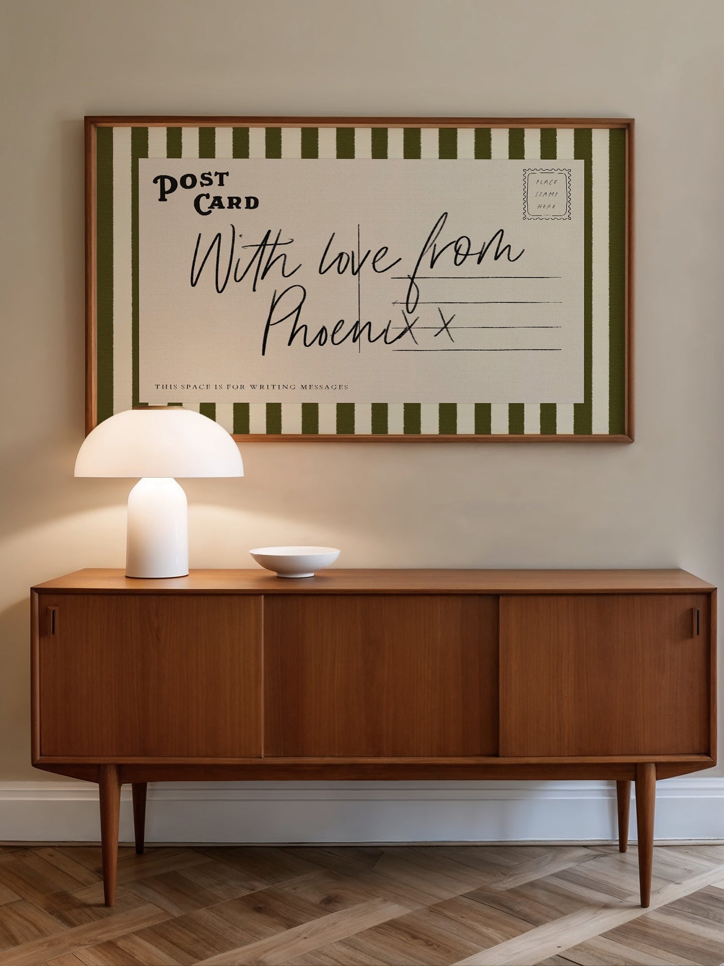 a wooden cabinet with a white lamp on top, and a framed postcard hanging on the wall above it.