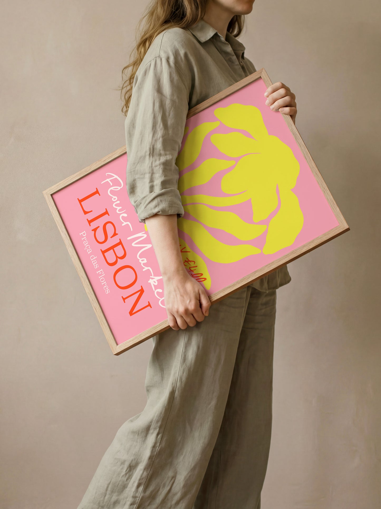 A woman is holding a framed poster with a pink background and a yellow flower design.