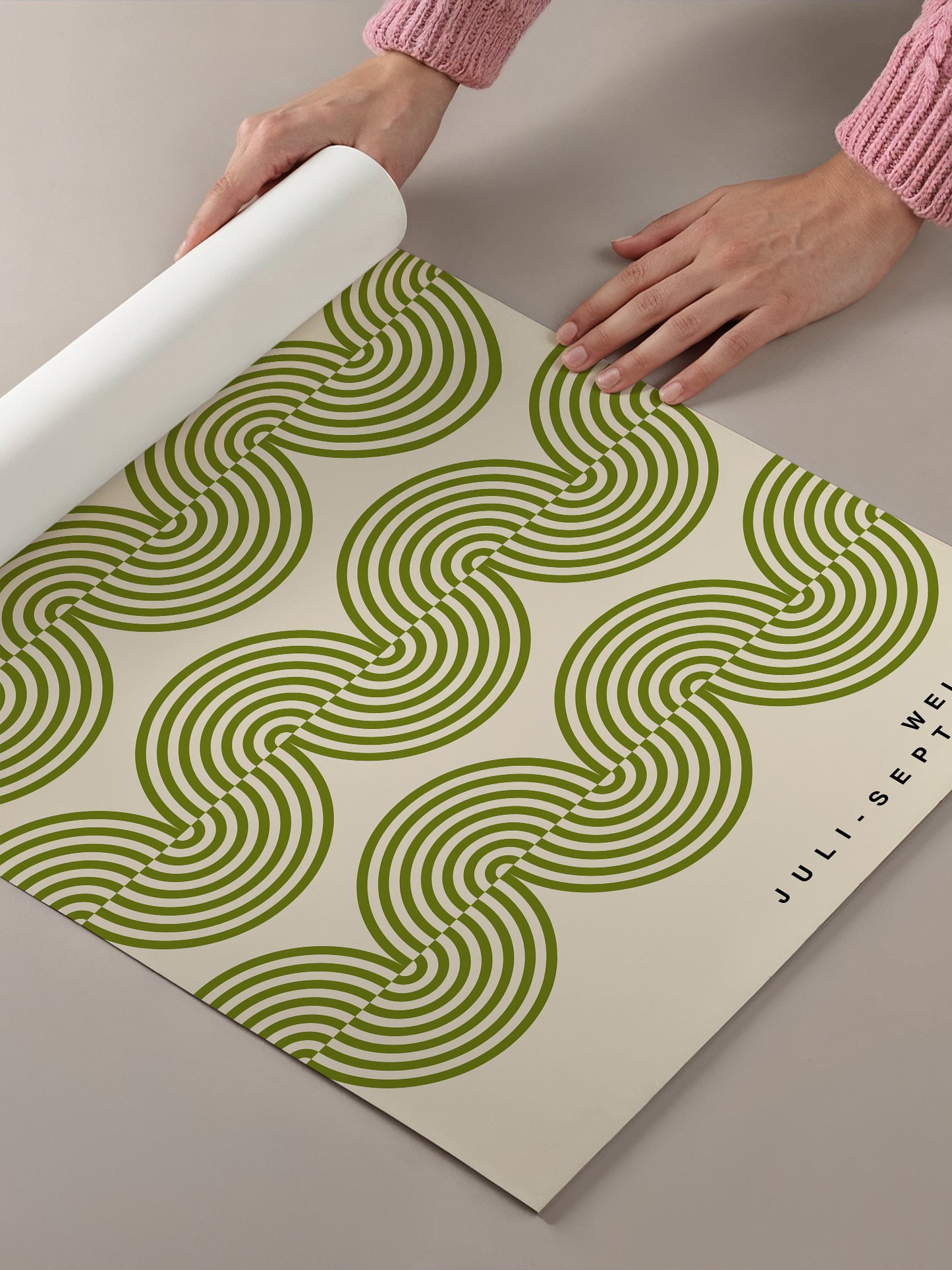 A person's hands are rolling out a piece of paper with a repeating pattern of green and white swirls.