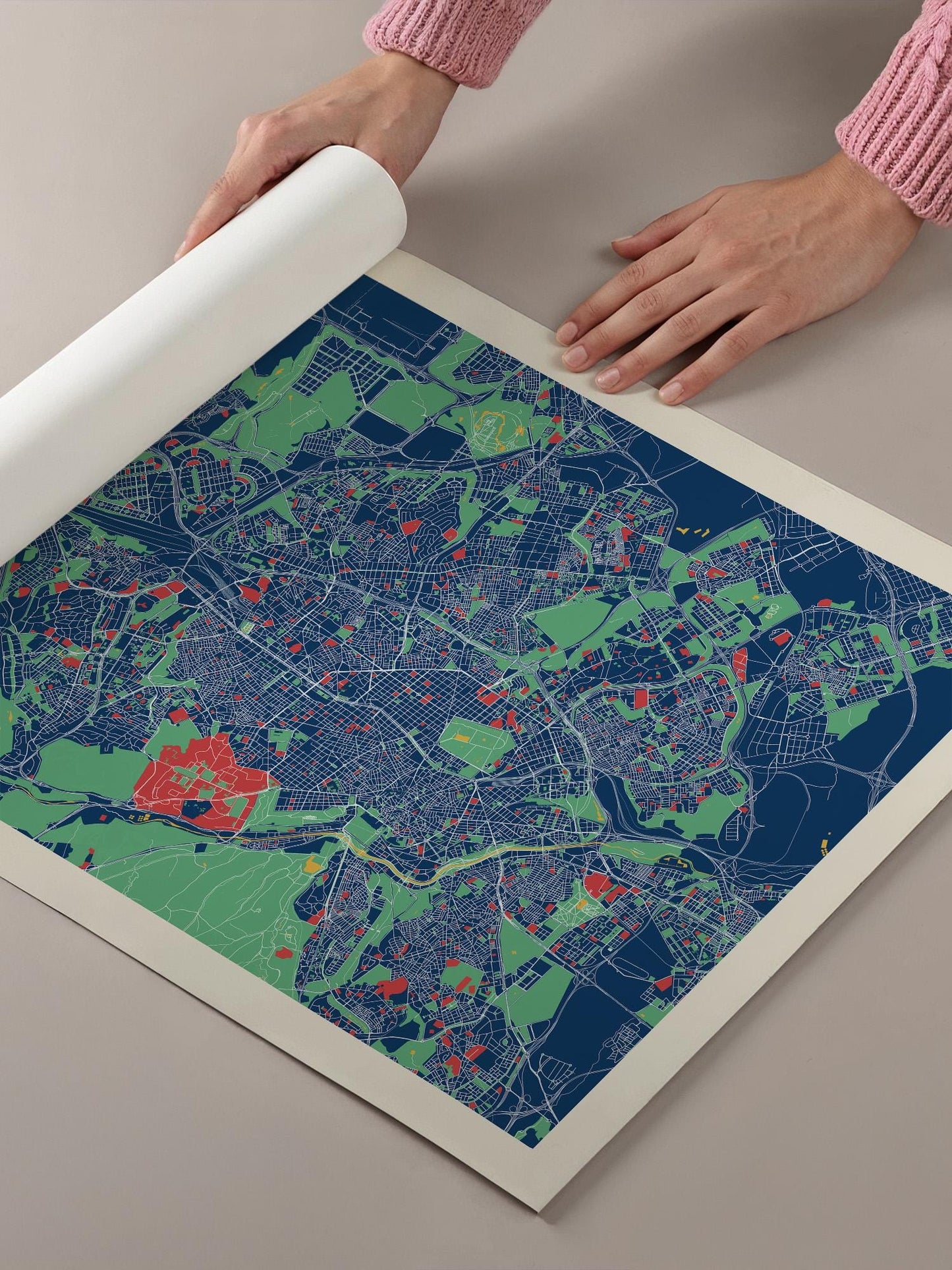 A person's hands are holding a roll of paper over a colorful map of a city, which appears to be a detailed and vibrant representation of the urban landscape.