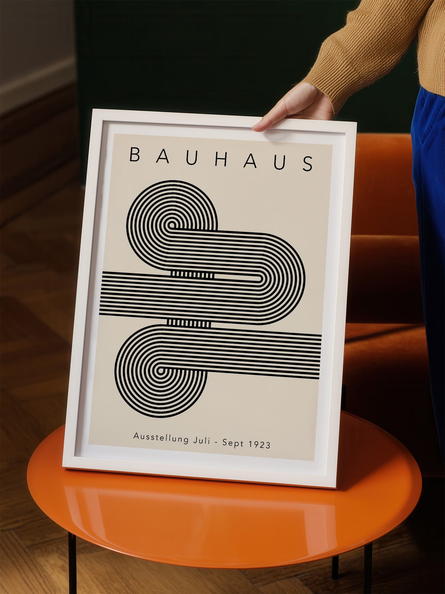 A person is holding a framed poster of the Bauhaus art style, featuring a minimalist design with a repeating pattern of curved lines.