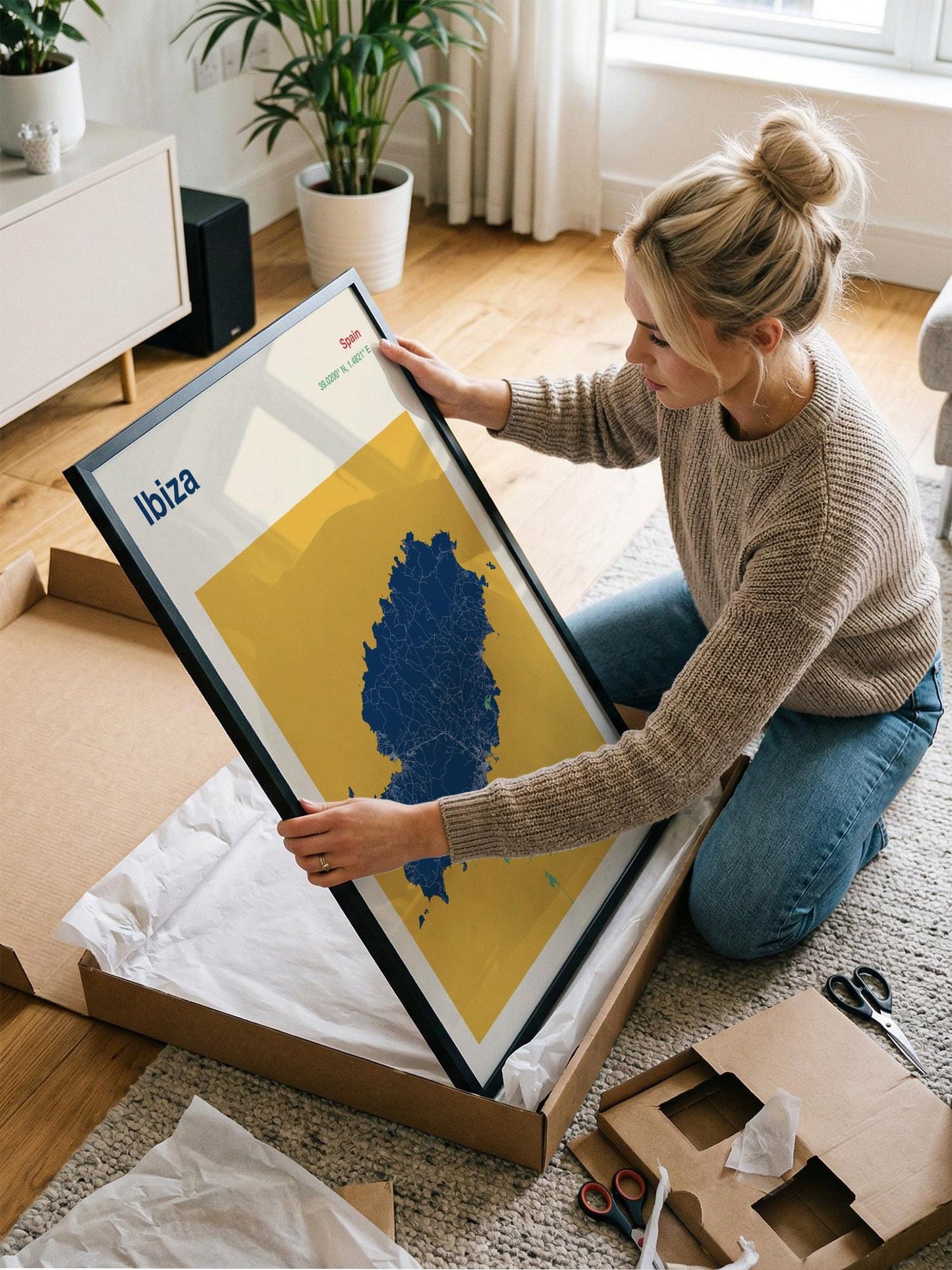 A woman is kneeling on the floor and holding a large framed picture with a map of Ibiza, Spain.