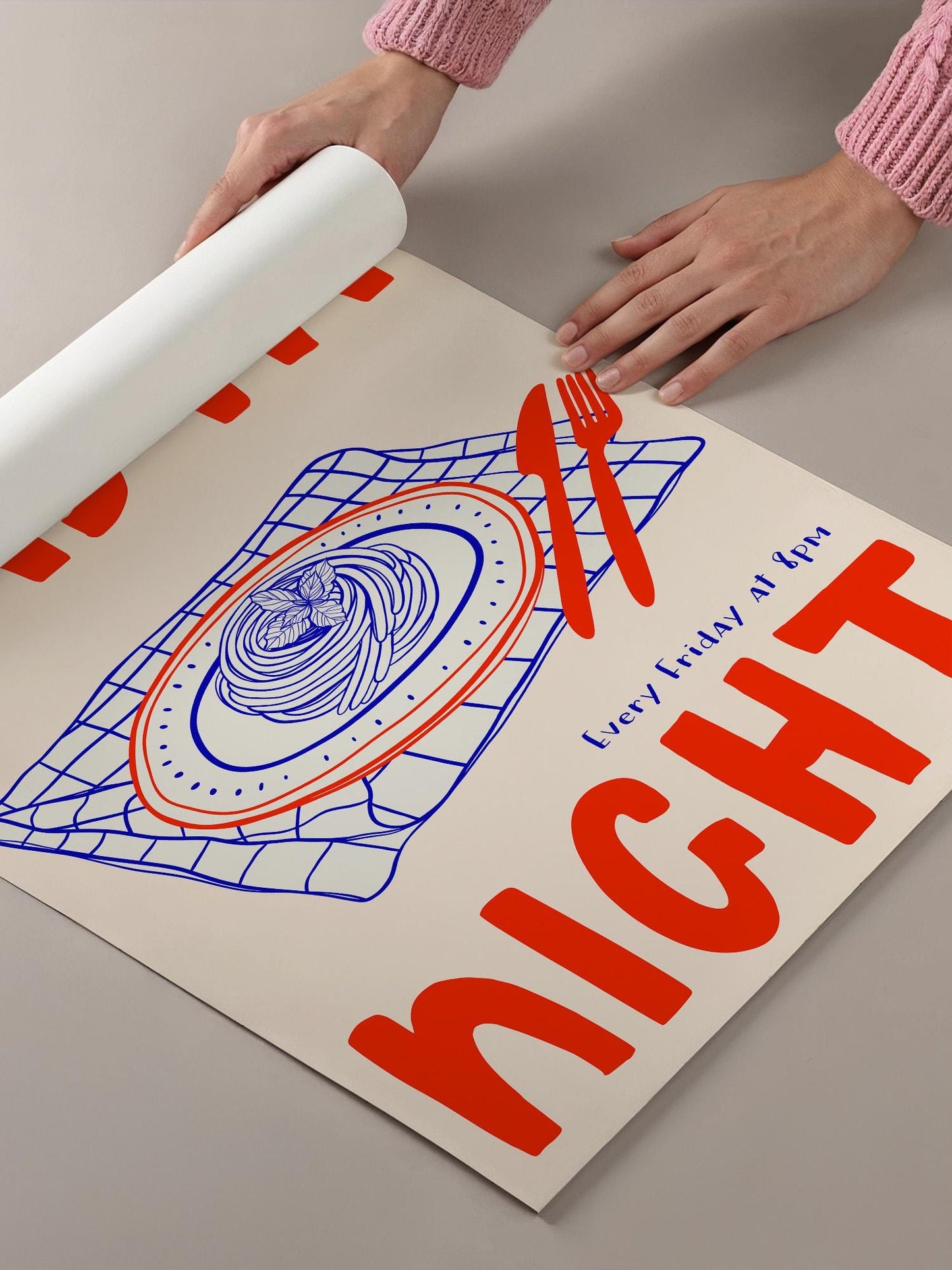 A person's hands are holding a roll of paper, which is being used to roll out a poster or a piece of paper. The poster features a large illustration of a plate with food, along with the text "Every Friday at night" written on it.