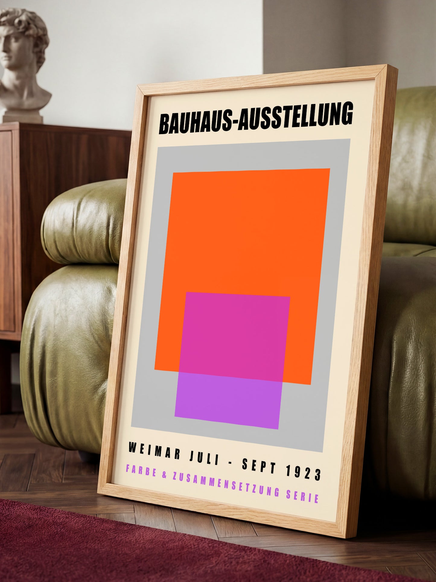 a poster for the Bauhaus-Ausstellung exhibition, which took place in Bauhaus, Germany from September 1923 to September 1926. The poster is displayed on a wooden stand, with a green leather couch visible in the background.
