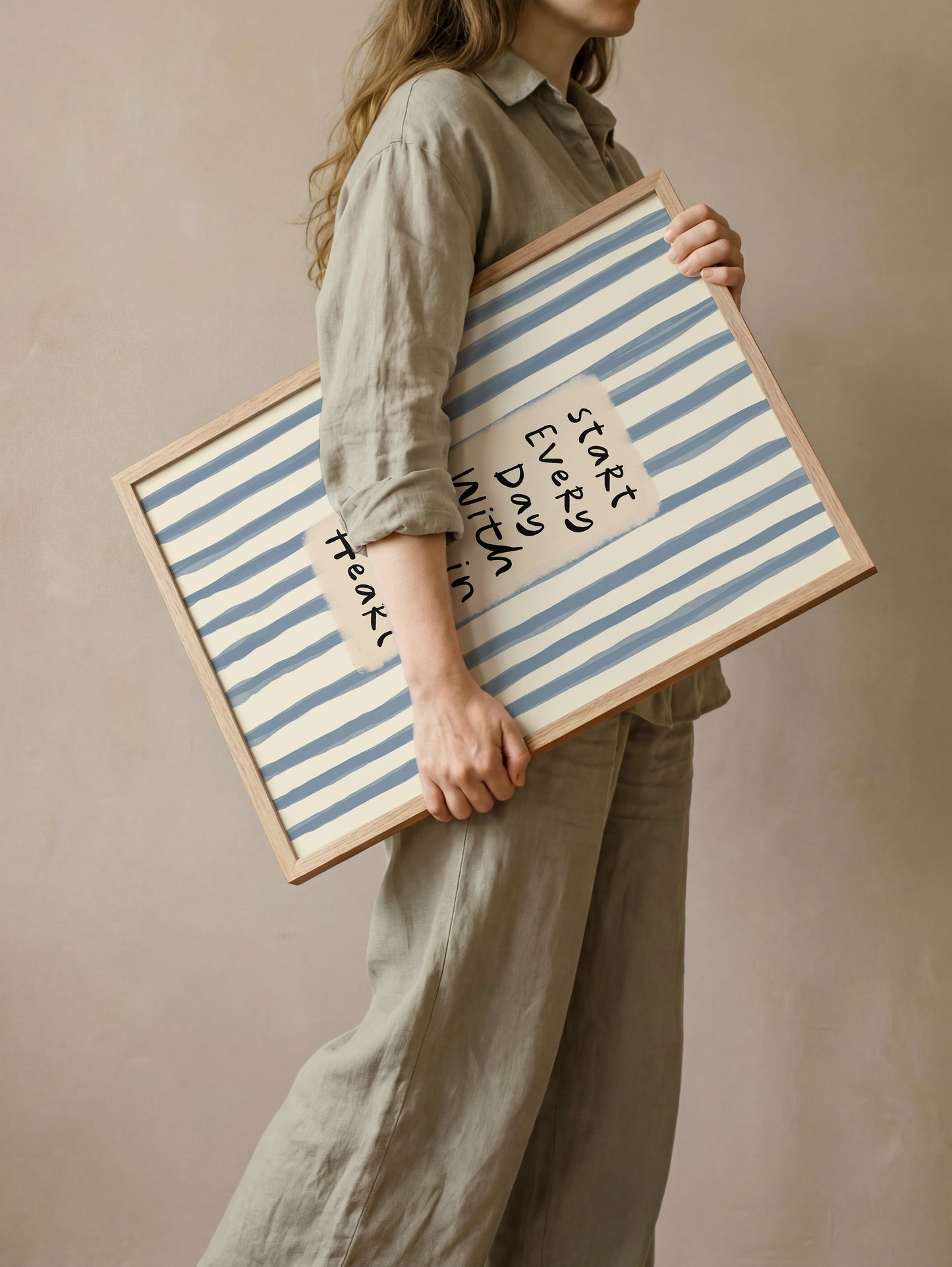 A woman is holding a large picture frame with a blue and white striped pattern.