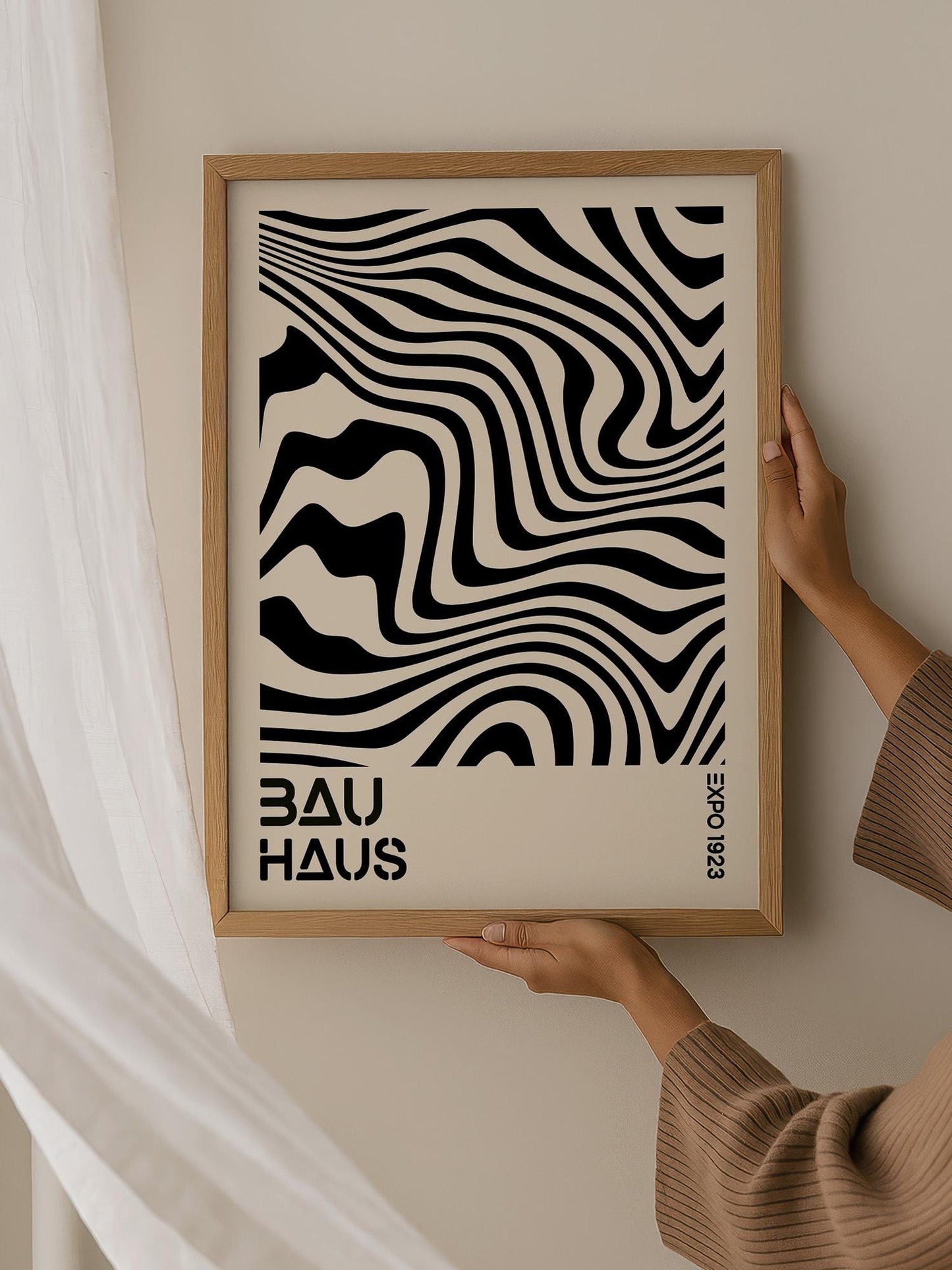 A person is holding up a framed poster with a black and white abstract design featuring wavy lines.