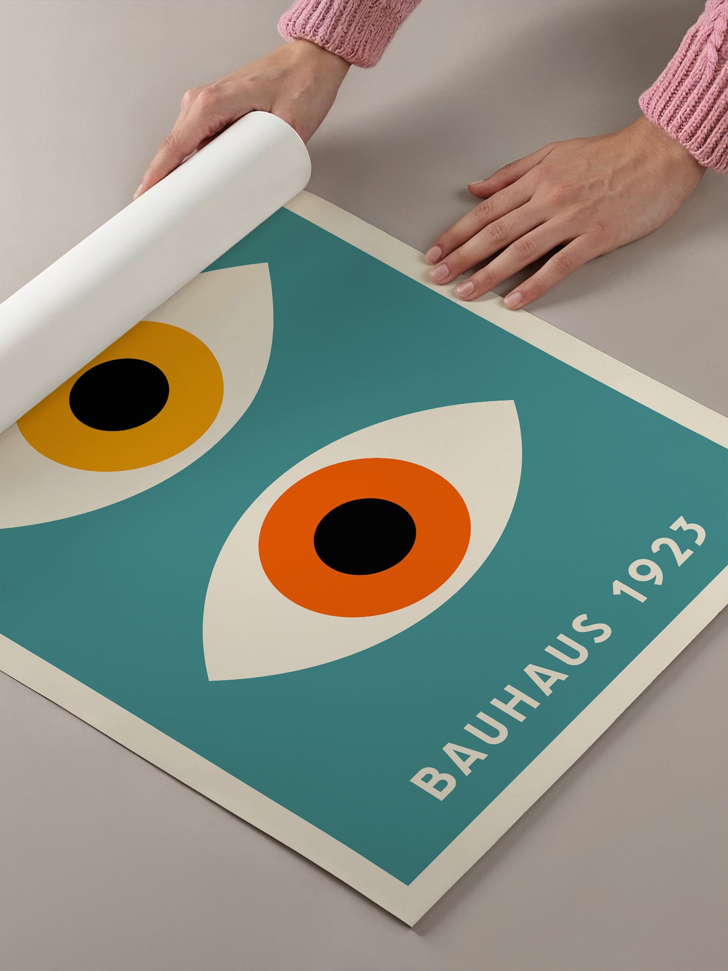 A person's hands are holding a roll of paper, which is placed on top of a poster featuring a stylized eye design in shades of blue and orange.