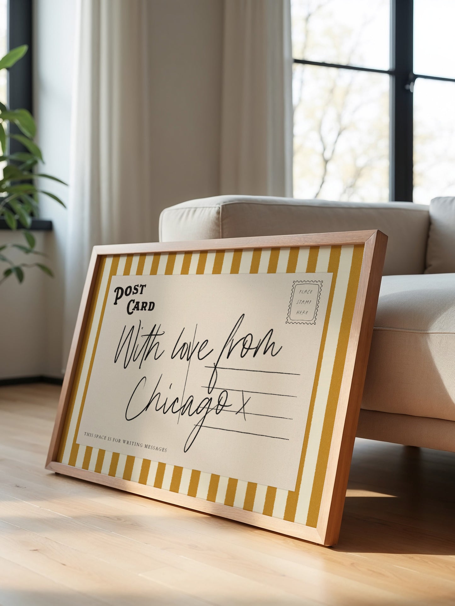 A framed postcard with handwritten text is leaning against a white couch in a room with a window.