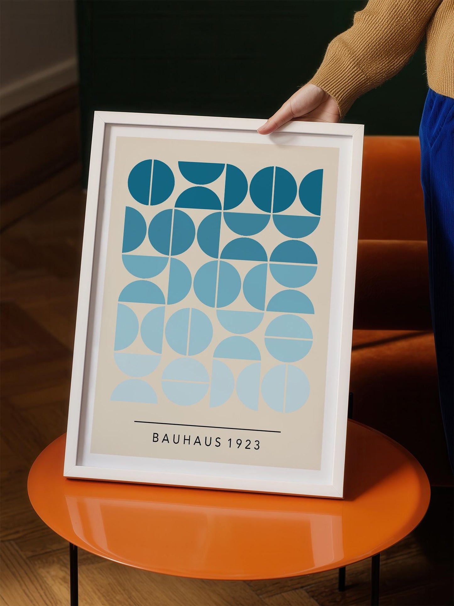 A person is holding up a framed print with a geometric design featuring blue circles and lines.